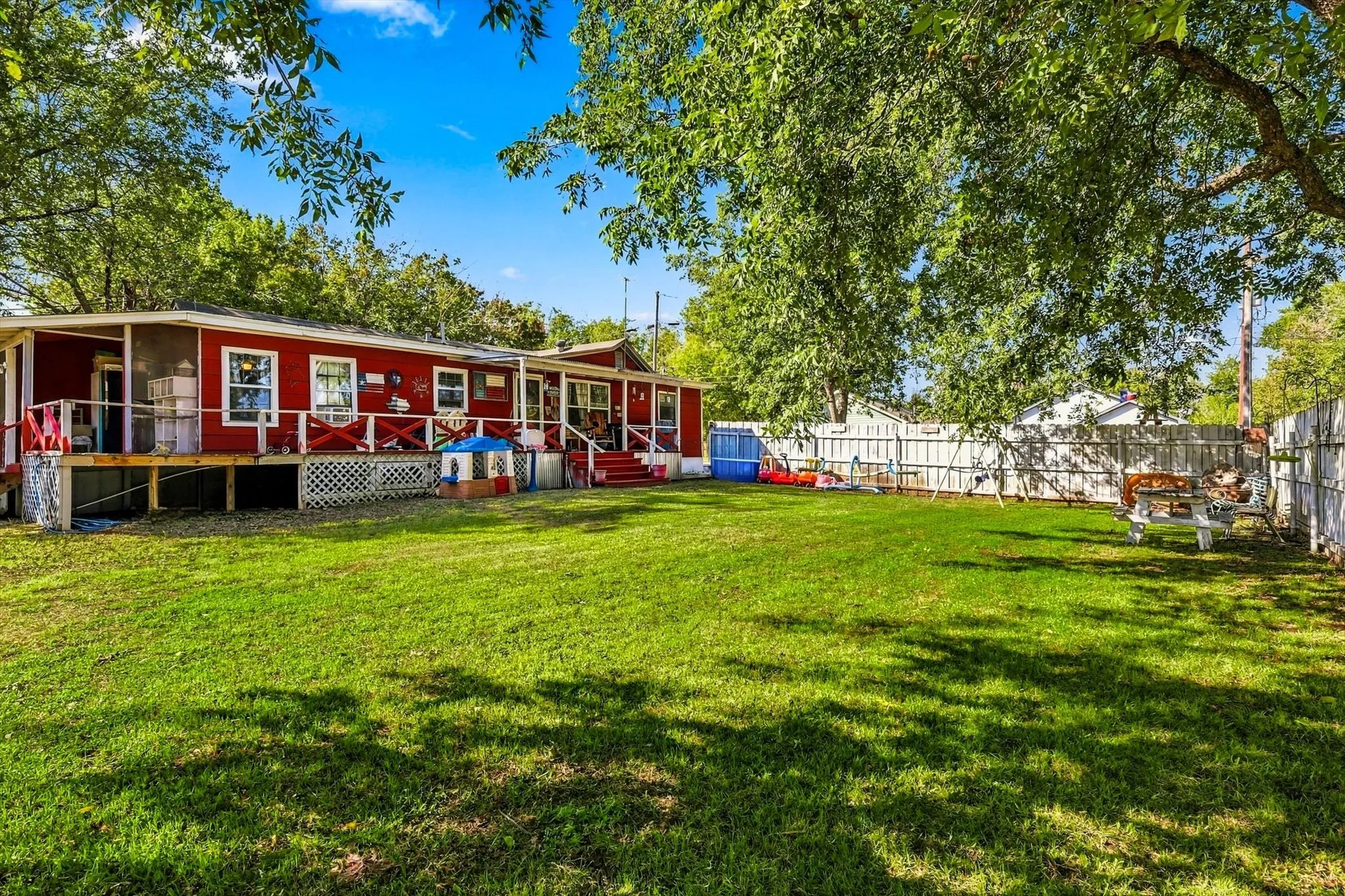Expansive backyard featuring a large grass lawn, perimeter wood fencing, mature shade trees, and an elevated deck with lattice skirting