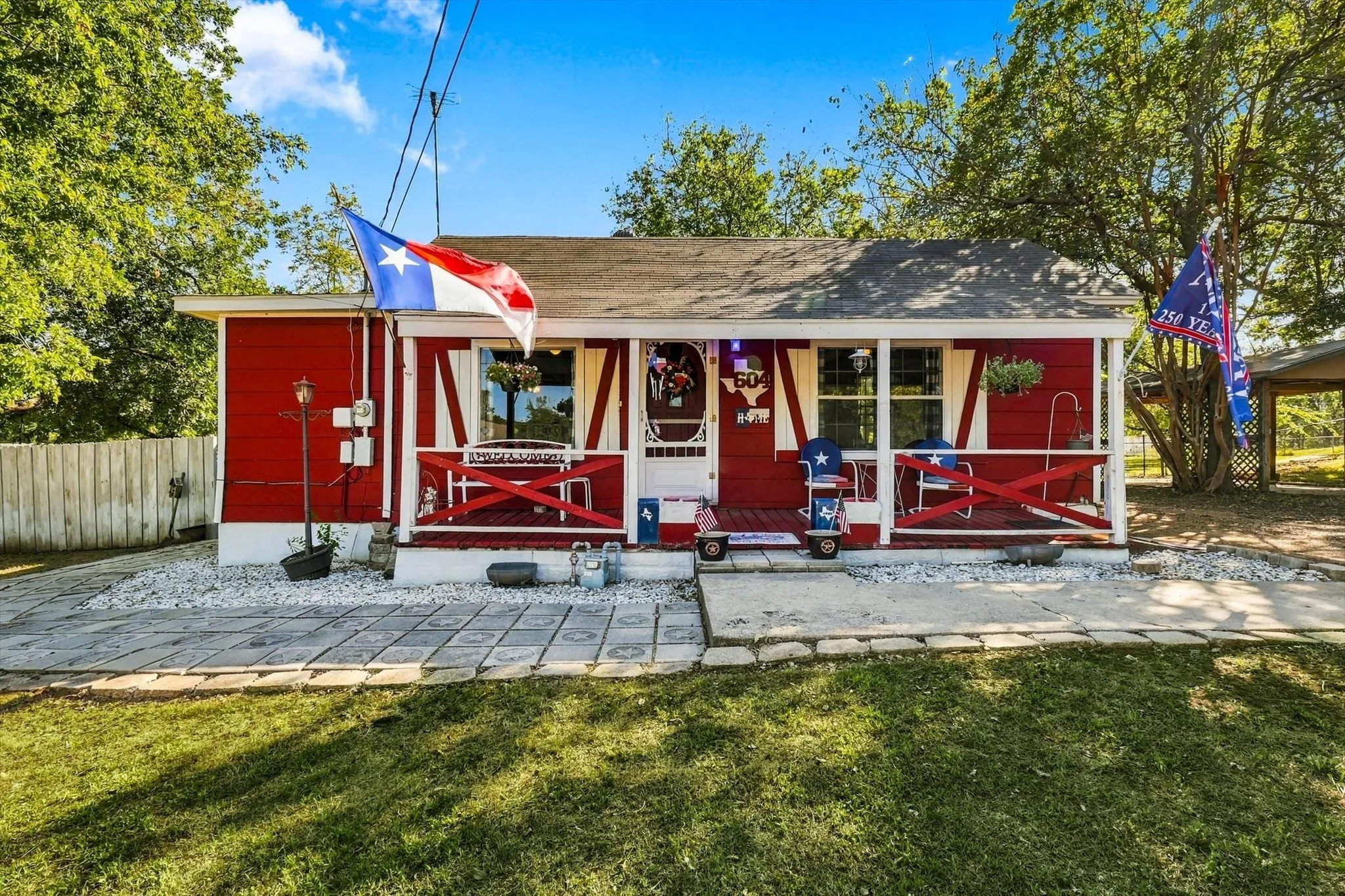 Single-story exterior featuring wood-style siding, a covered front porch with cross-buck railing, and concrete paver hardscaping