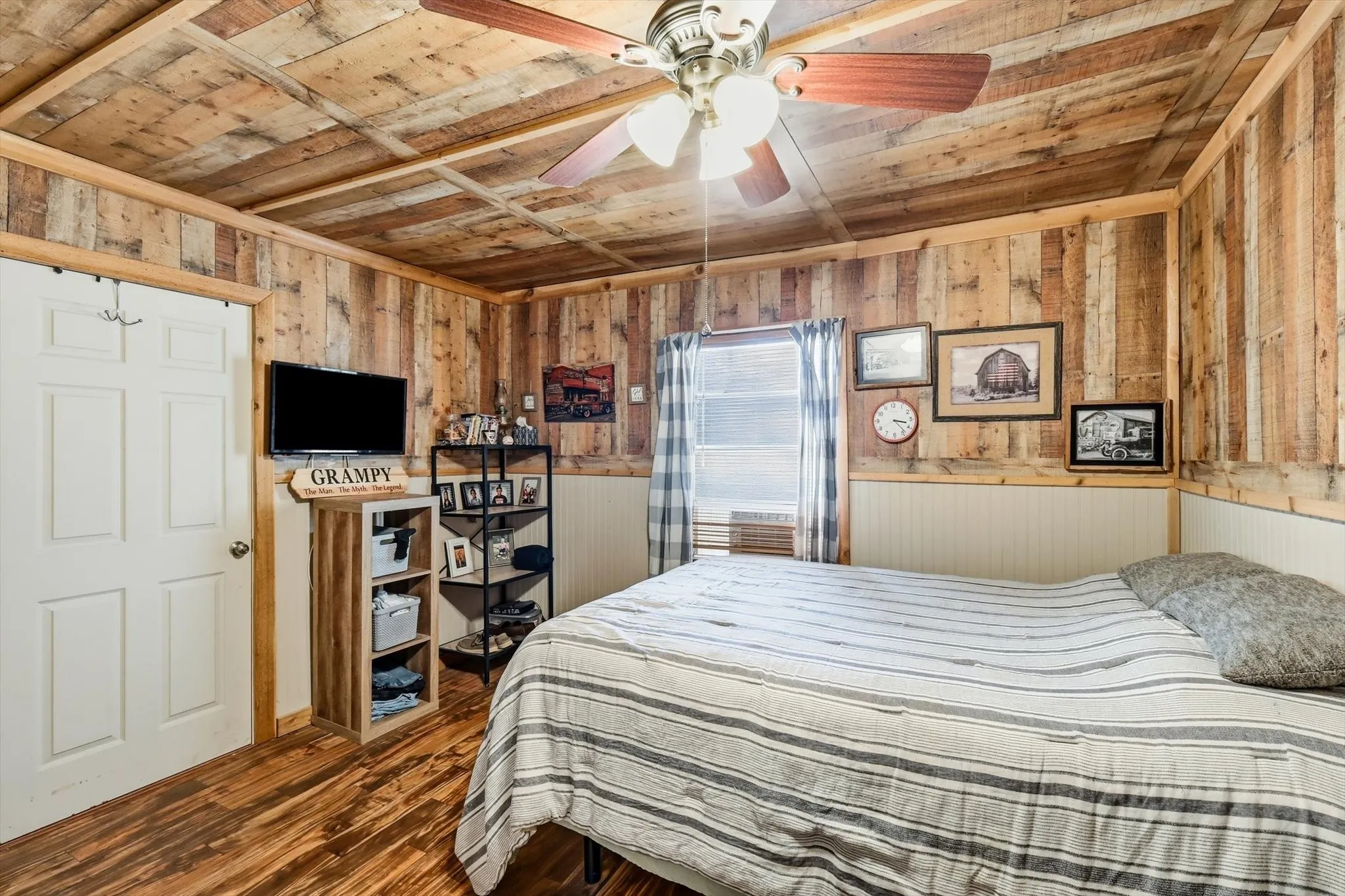 Vertical wood-plank wall paneling with exposed wood ceiling beams, wood-finish flooring, half-wall beadboard wainscoting, and a multi-blade ceiling fan with integrated lighting