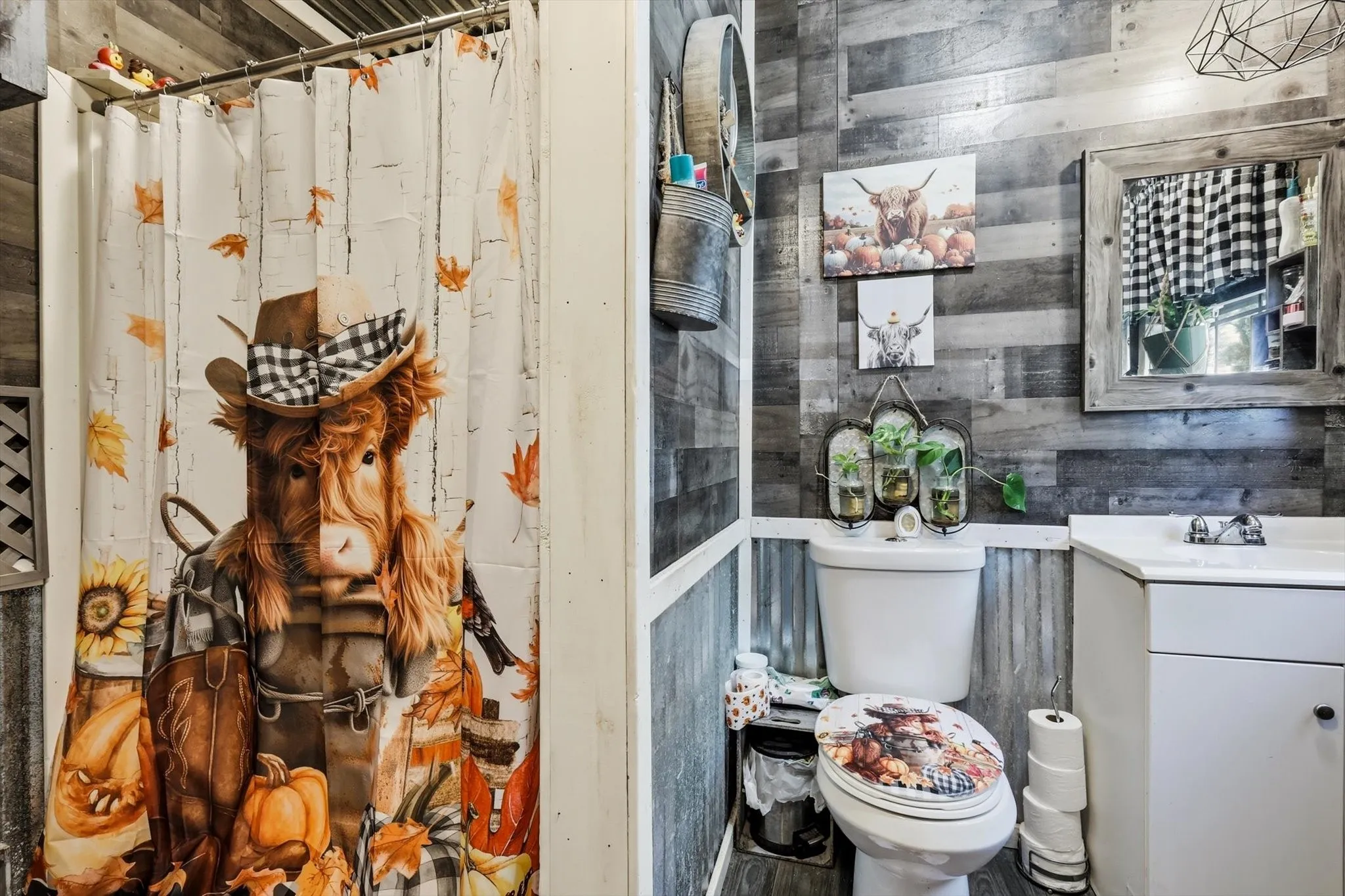 Bathroom featuring horizontal wood-plank walls, corrugated metal wainscoting, a white vanity cabinet, a framed mirror, and a geometric pendant light fixture
