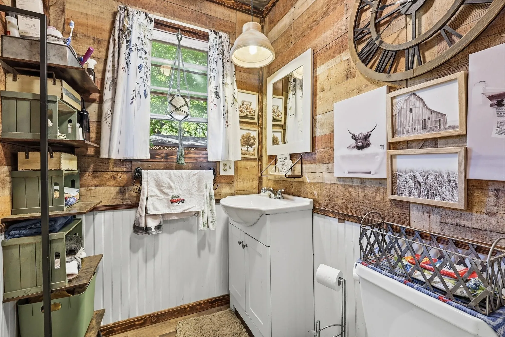 Bathroom featuring reclaimed wood wall paneling, lower white wainscoting, pedestal-style vanity with white cabinetry, and a single pendant light fixture