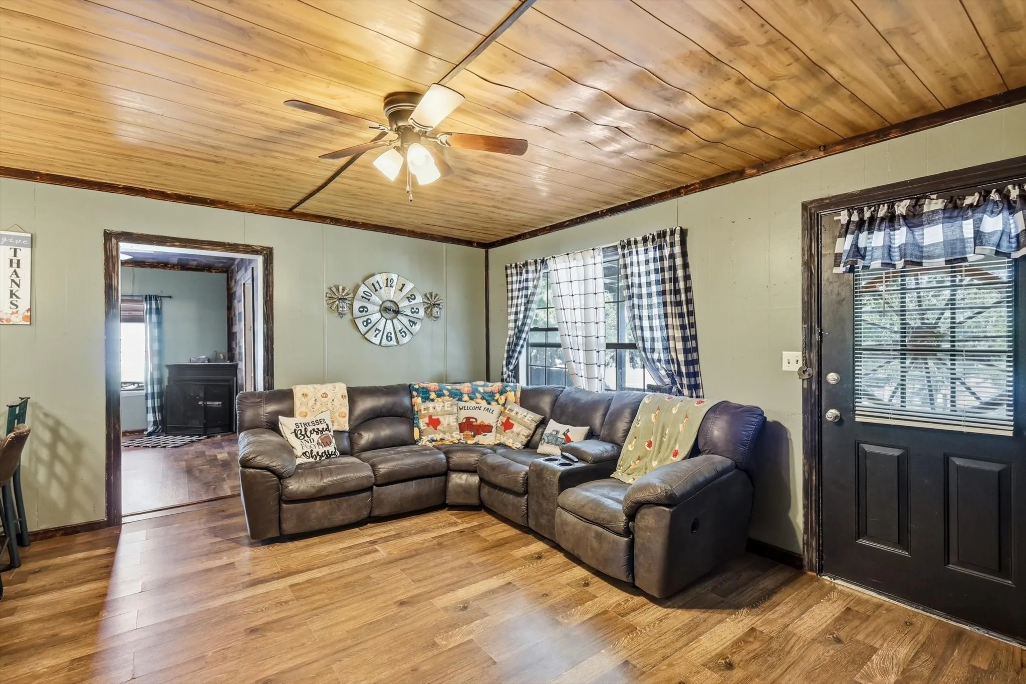 Living area featuring wood-plank ceiling, wood-finish flooring, dark-trimmed doorways, and a flush-mount ceiling fan with integrated lighting