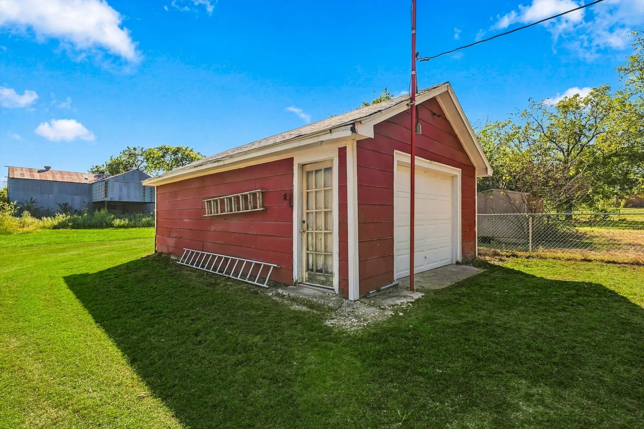 Detached single-car garage featuring red horizontal siding, a gabled roofline, a white overhead door, and a multi-pane glass-panel entry door