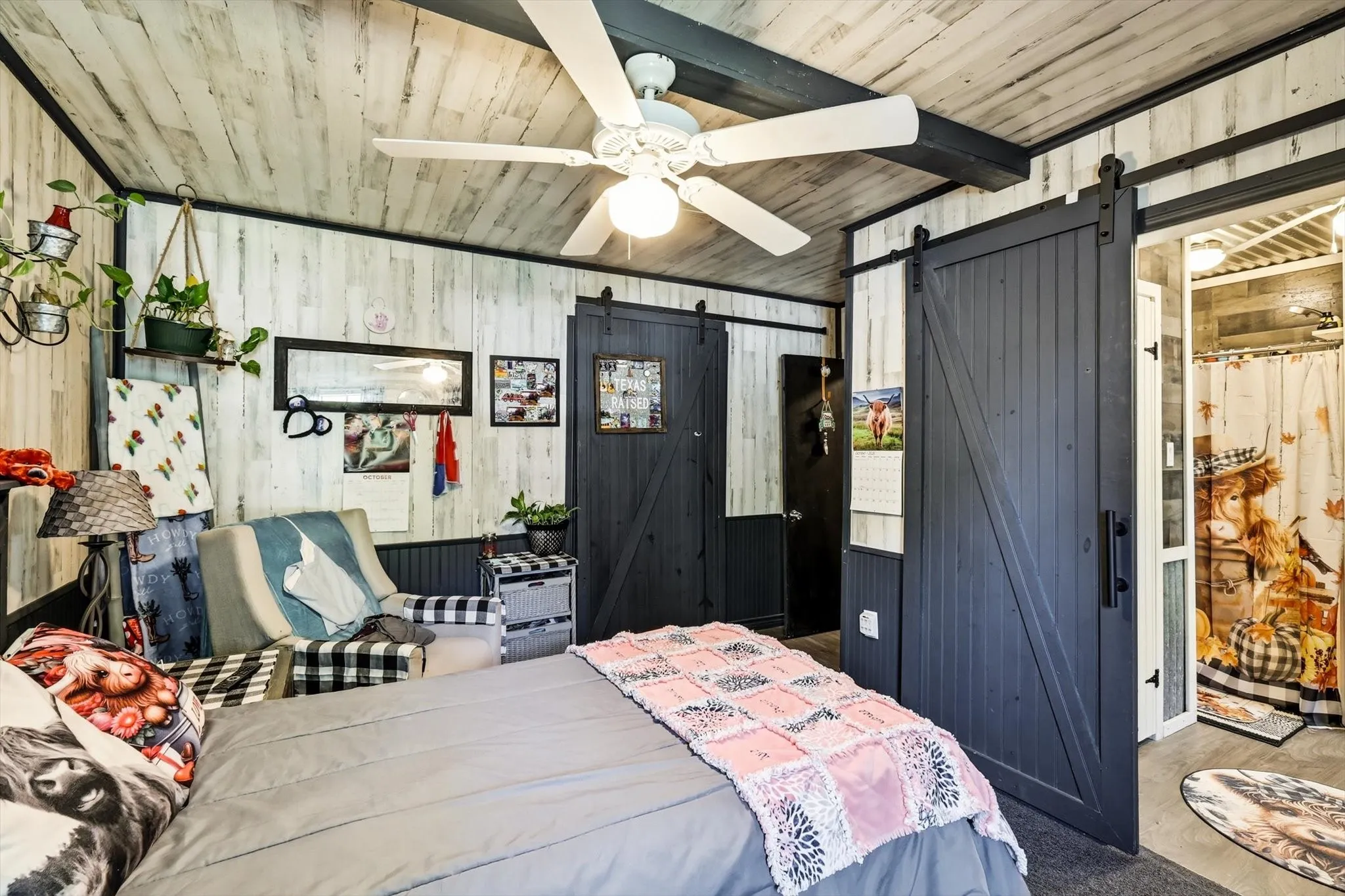 Interior featuring whitewashed wood-plank walls and ceiling, dark-toned sliding barn doors with matte black hardware, and an overhead ceiling fan with integrated lighting