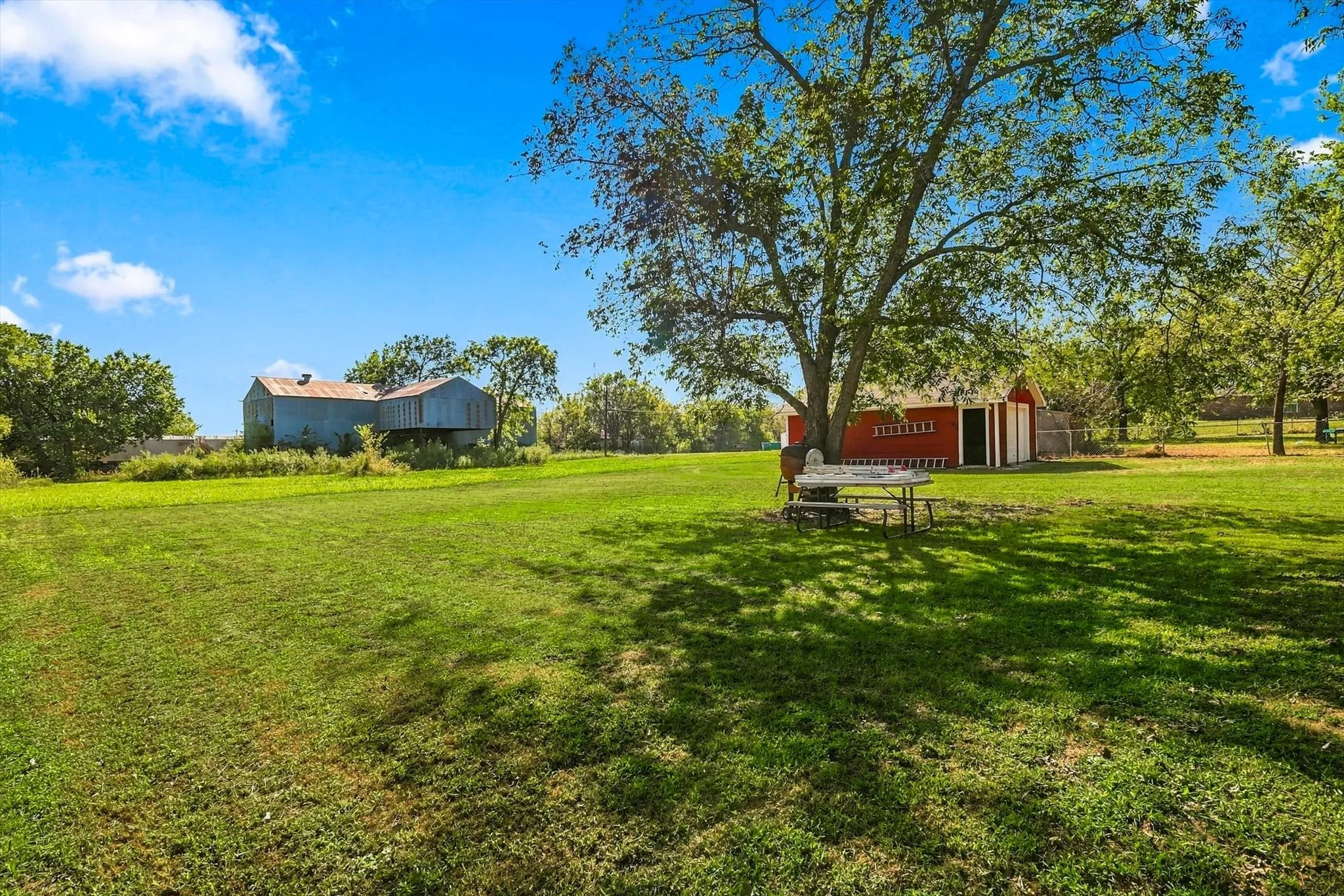Expansive acreage featuring a manicured lawn, mature trees, a detached red barn, and a metal-sided outbuilding