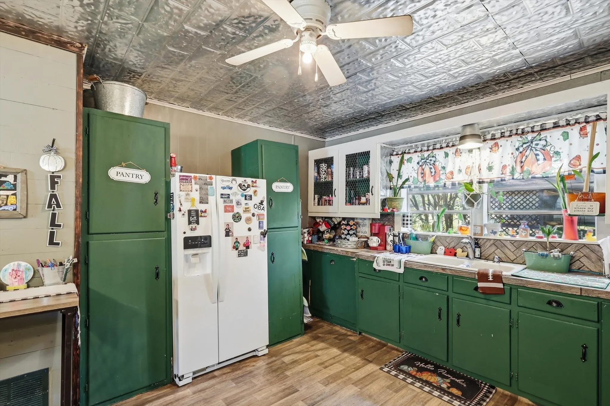 Kitchen featuring a decorative pressed-tin ceiling, green built-in cabinetry, wood-finish flooring, a farmhouse-style sink, and a herringbone-patterned tile backsplash