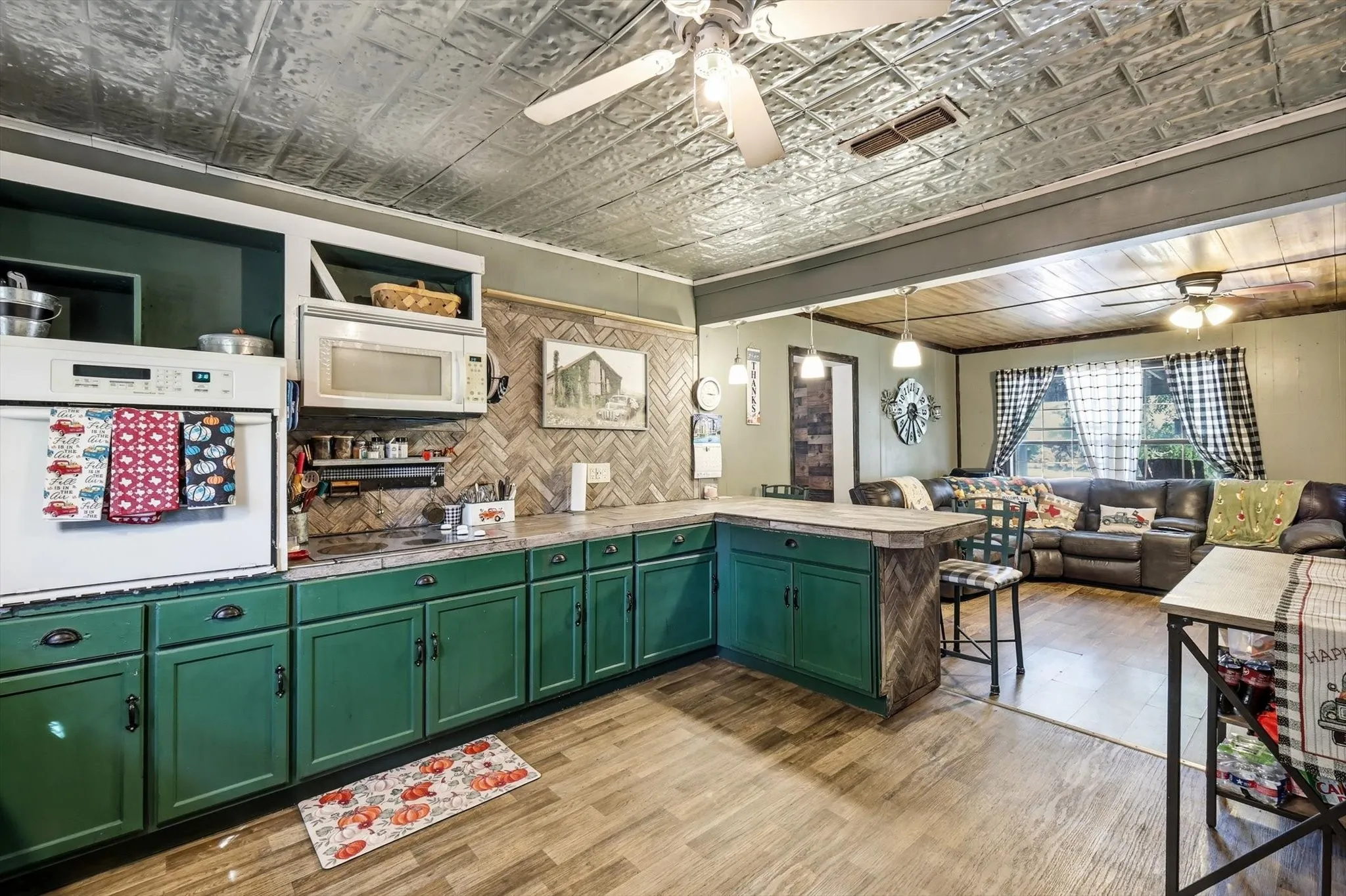 Kitchen featuring green cabinetry, herringbone pattern backsplash, metallic-finish coffered ceiling, wood-finish flooring, and a breakfast bar