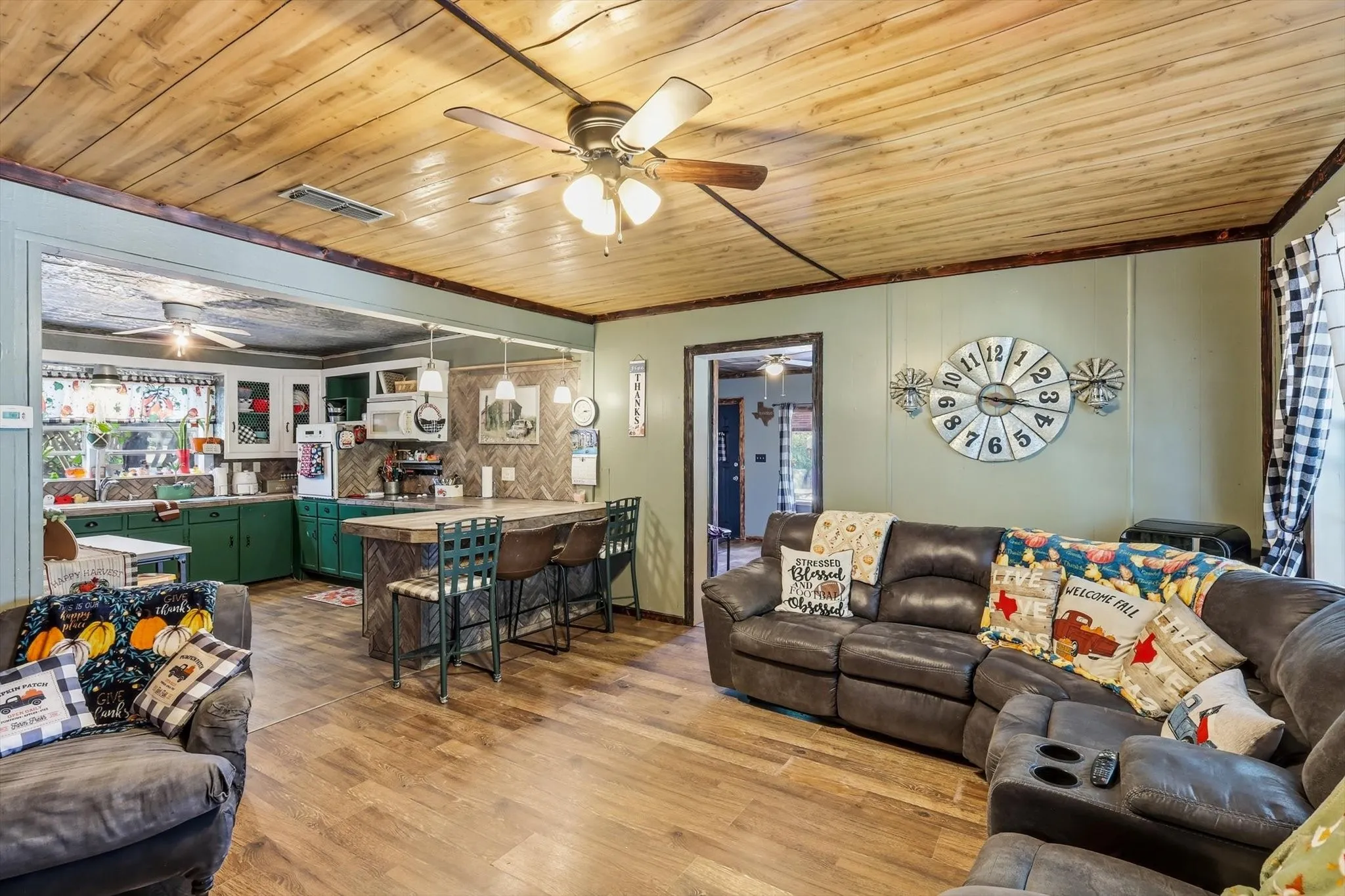 Natural wood plank ceiling featuring a central multi-blade ceiling fan, wood-finish flooring, and a kitchen island with a decorative herringbone pattern finish
