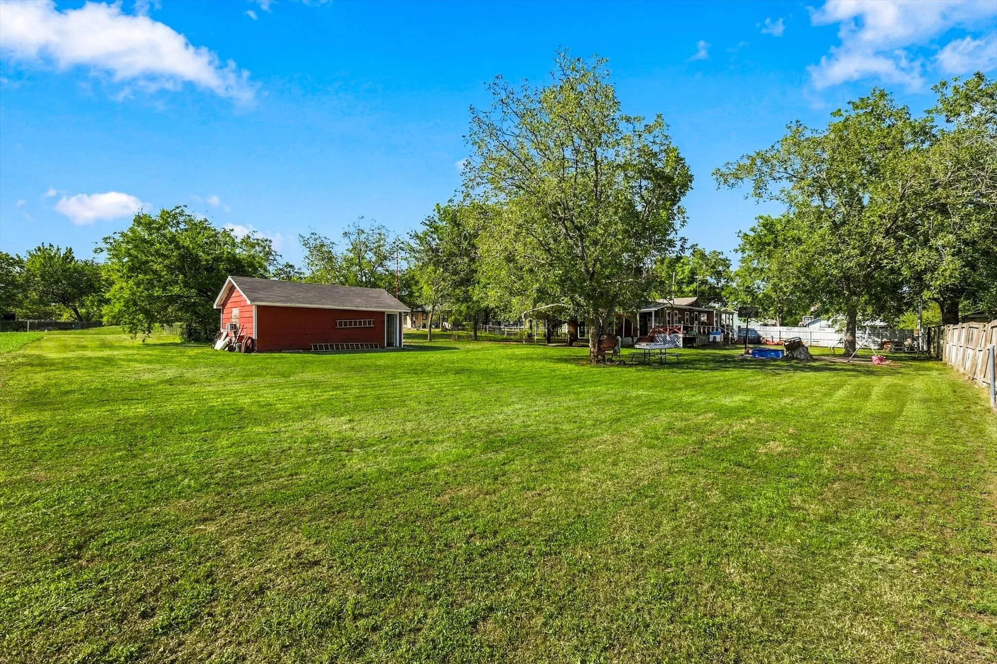 Expansive lot featuring a detached red siding structure, mature trees, and wooden perimeter fencing