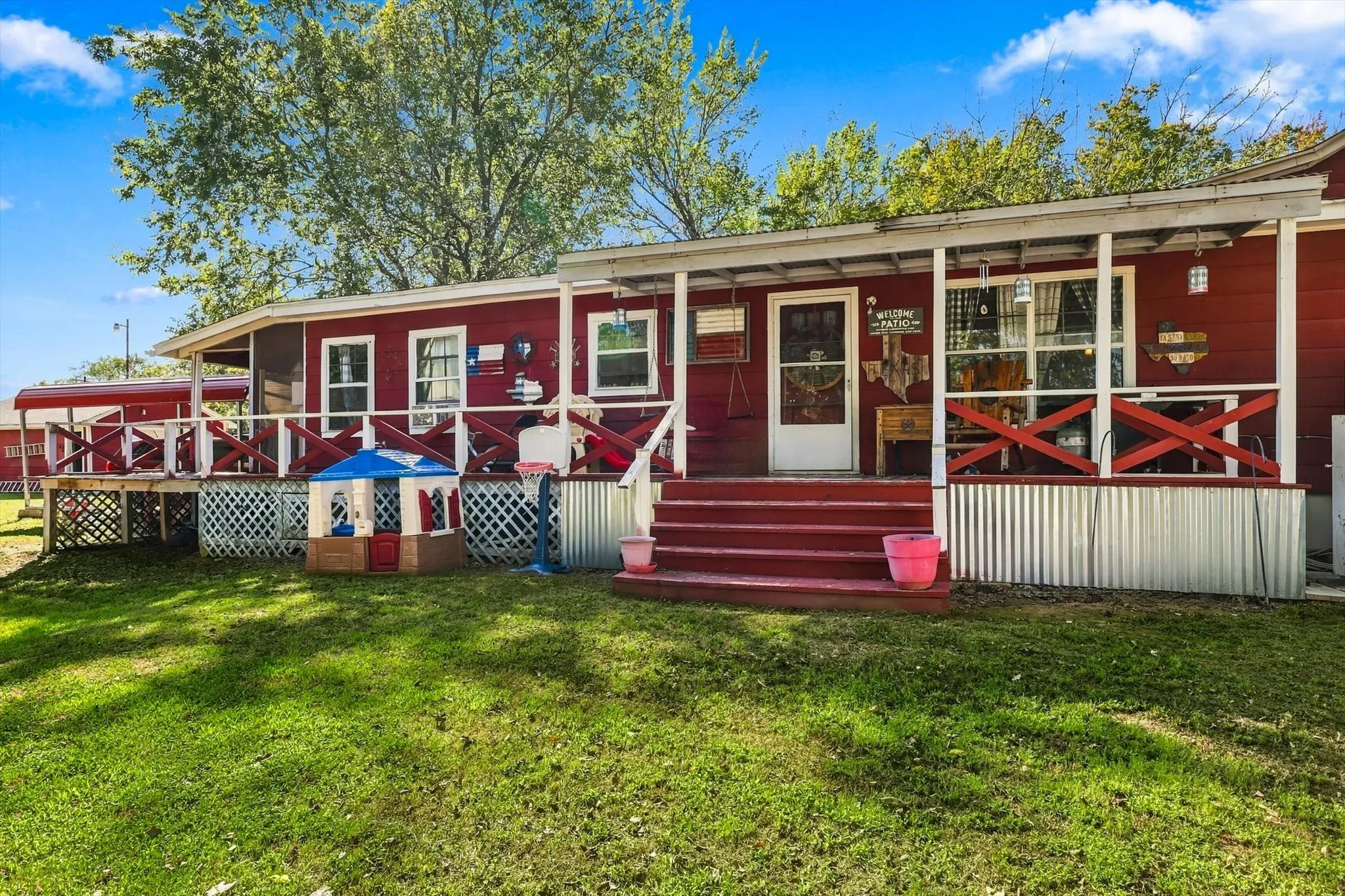 Extended covered front porch with red wooden railings and a corrugated metal skirting base