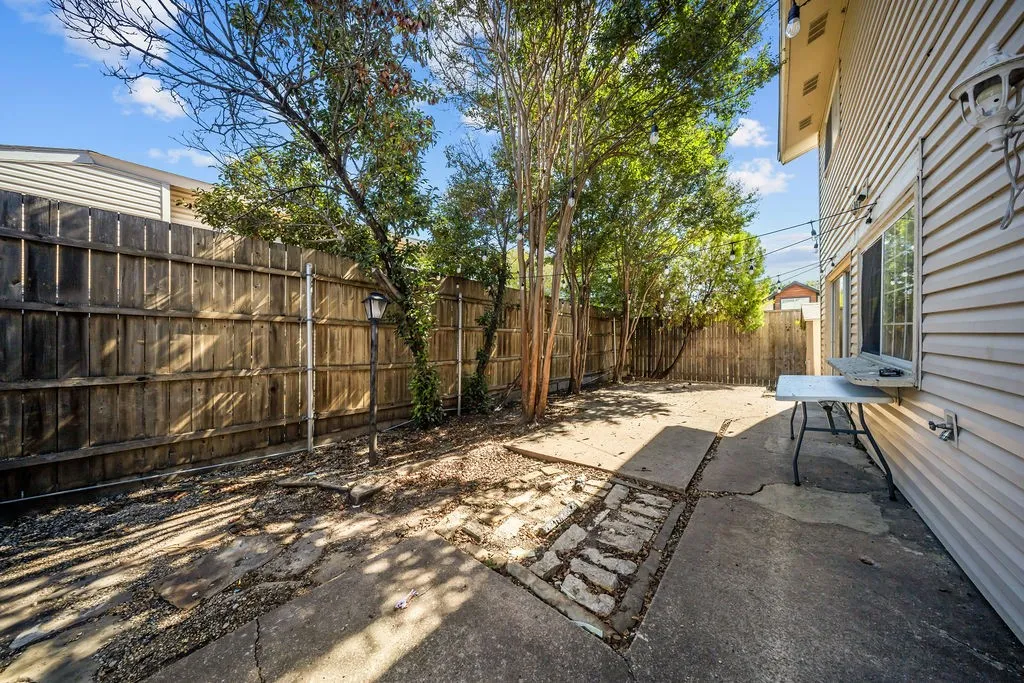 Backyard featuring a wood privacy fence, concrete patio area, mature trees, and vinyl siding exterior