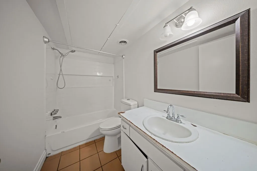 Bathroom featuring a vanity with an integrated basin, a combination tub and shower with a handheld sprayer, tiled flooring, and a wall-mounted light fixture above the vanity mirror