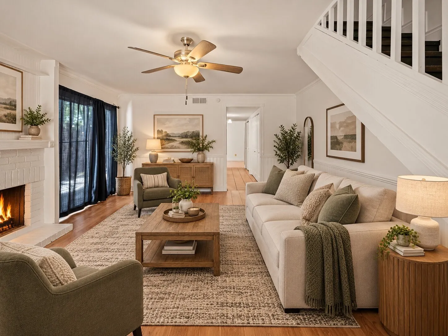 Living area featuring wood-finish flooring, a painted brick fireplace, a central ceiling fan, and a staircase with a white balustrade