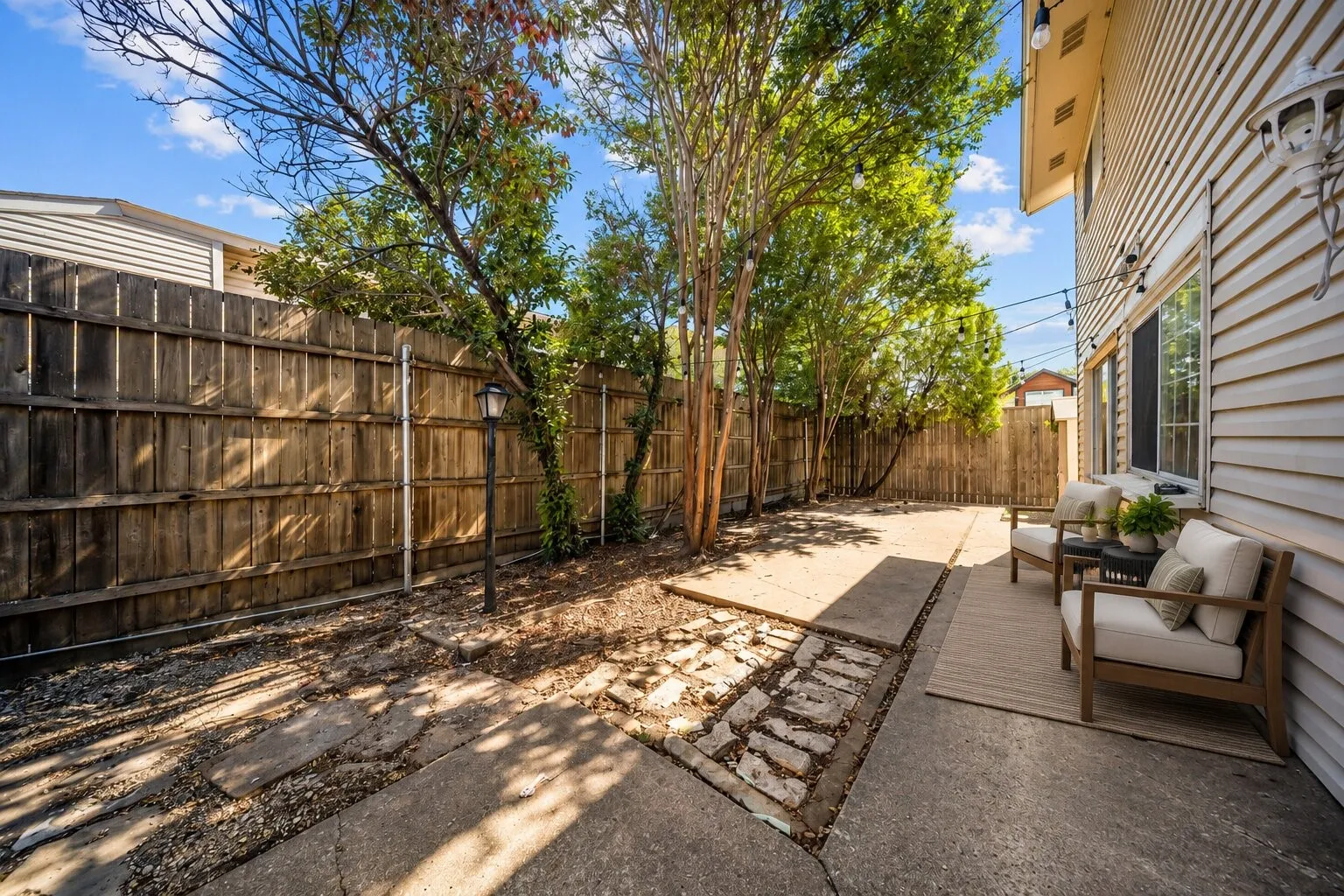 Concrete patio, wood-slat privacy fencing, established mature trees, and overhead string lighting