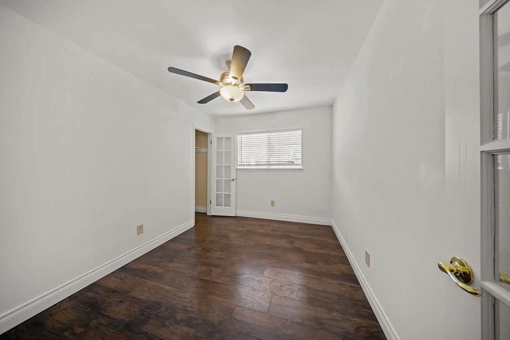Room featuring wood-finish flooring, a ceiling fan with integrated lighting, a multi-pane glass door, and a window with horizontal blinds