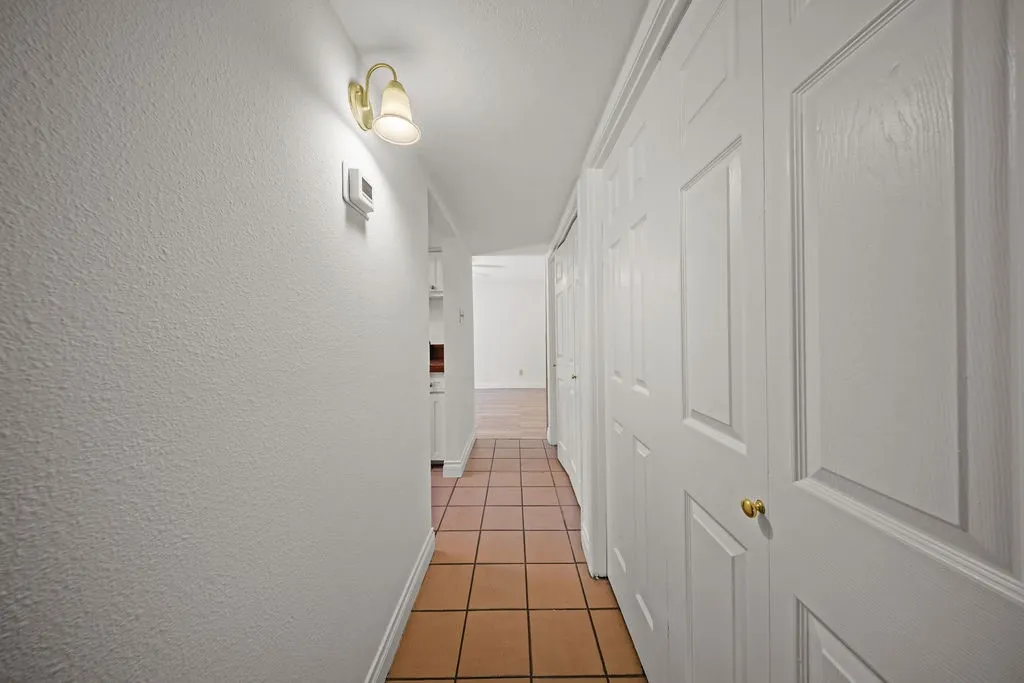 Ceramic tile flooring, white bi-fold closet doors, wall-mounted light fixture with frosted glass shade, and textured wall finish