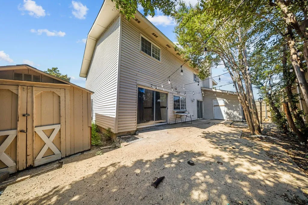Exterior rear elevation featuring light-toned vinyl siding, a concrete patio, and a detached wooden storage shed