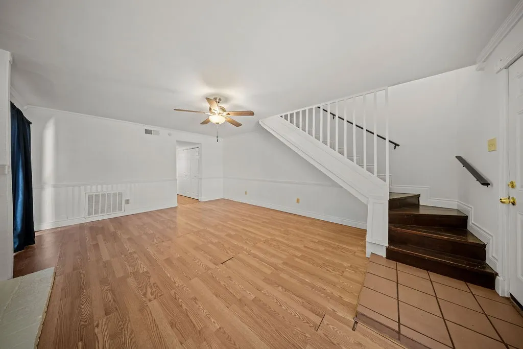 Open living area featuring wood-finish flooring, wainscoting, staircase with white railing, and ceiling fan