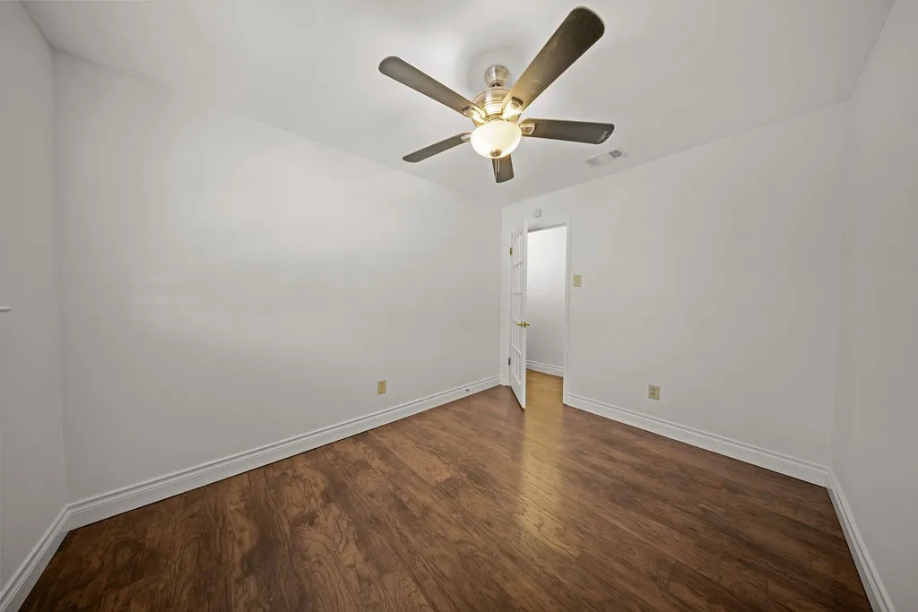 Room featuring dark wood-finish flooring, white walls, and a ceiling-mounted fan with integrated light fixture