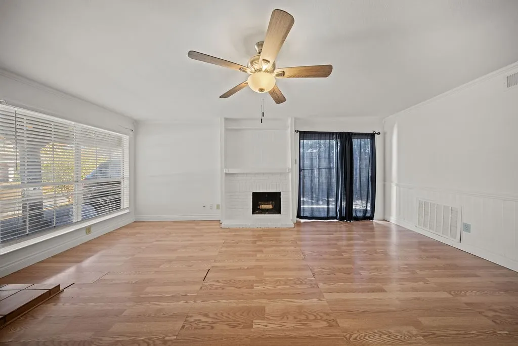 Interior space featuring wood-finish flooring, a painted brick fireplace with built-in shelving, a ceiling fan with integrated lighting, and horizontal window blinds