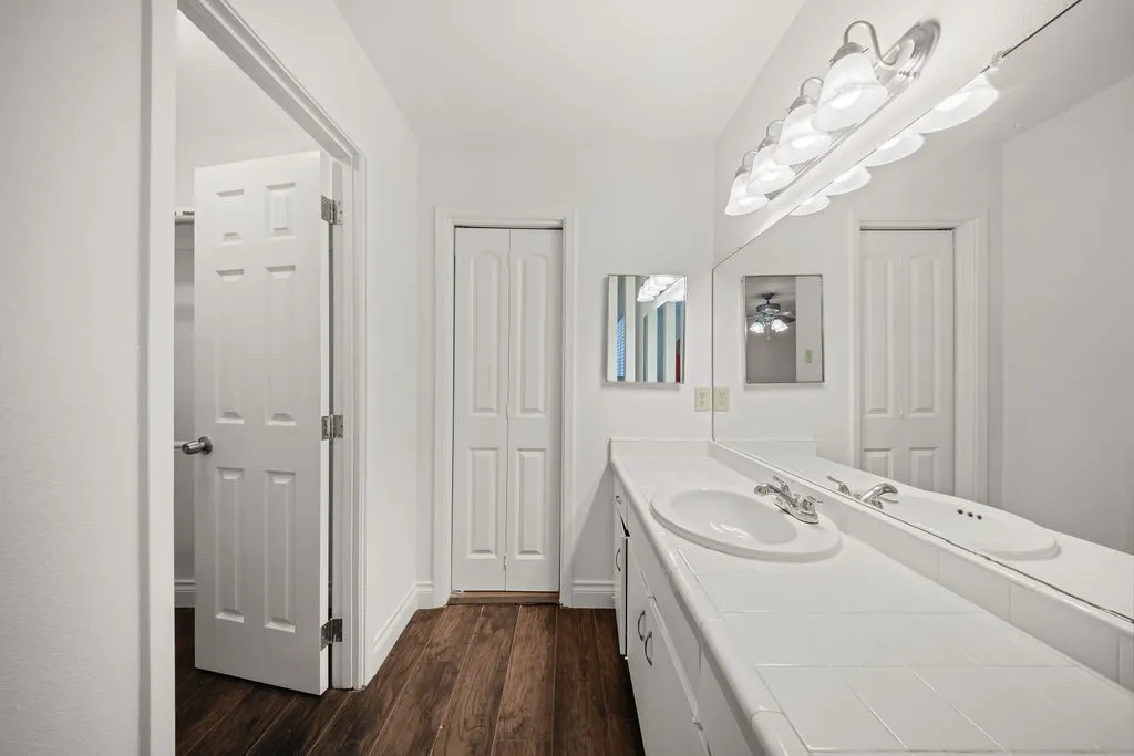 Vanity featuring a tile countertop, integrated oval basin, white cabinetry, wood-finish flooring, and a full-width wall mirror