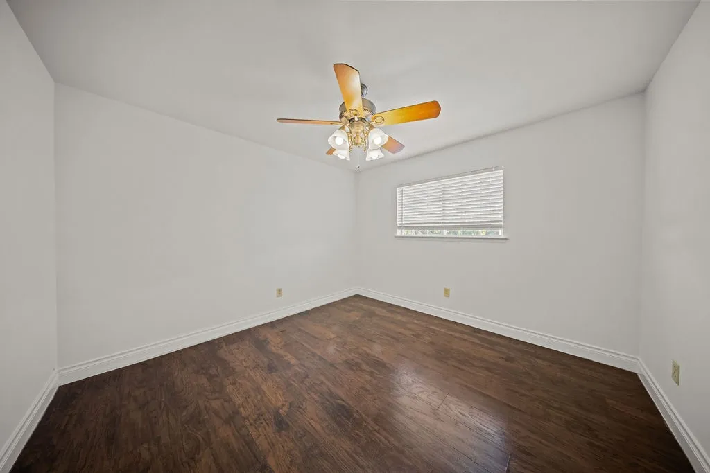 Room featuring wood-finish flooring, a ceiling fan with integrated lighting, and a window with horizontal blinds