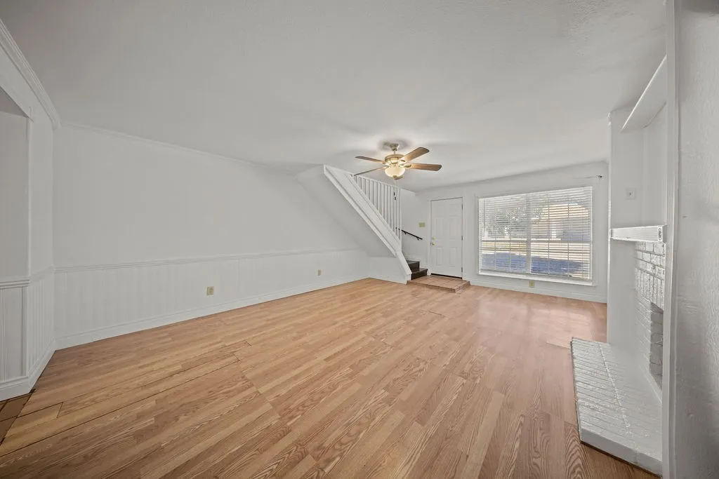 Living space featuring wood-finish flooring, white wainscoting, a painted brick fireplace, and a ceiling fan