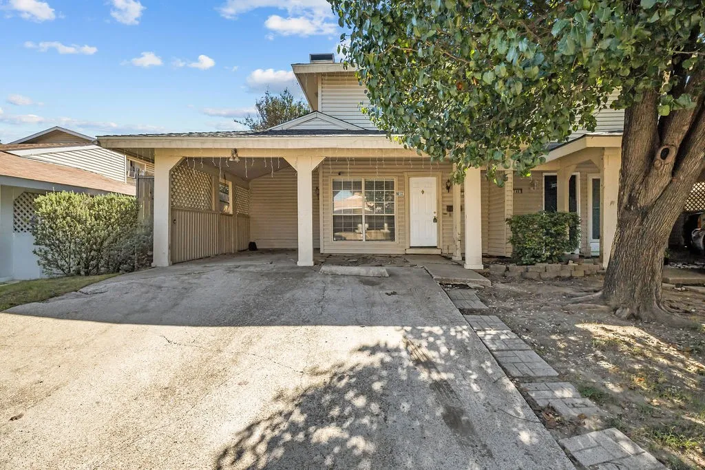 Two-story exterior featuring light-colored horizontal siding, an attached carport with decorative lattice privacy screening, and a concrete driveway