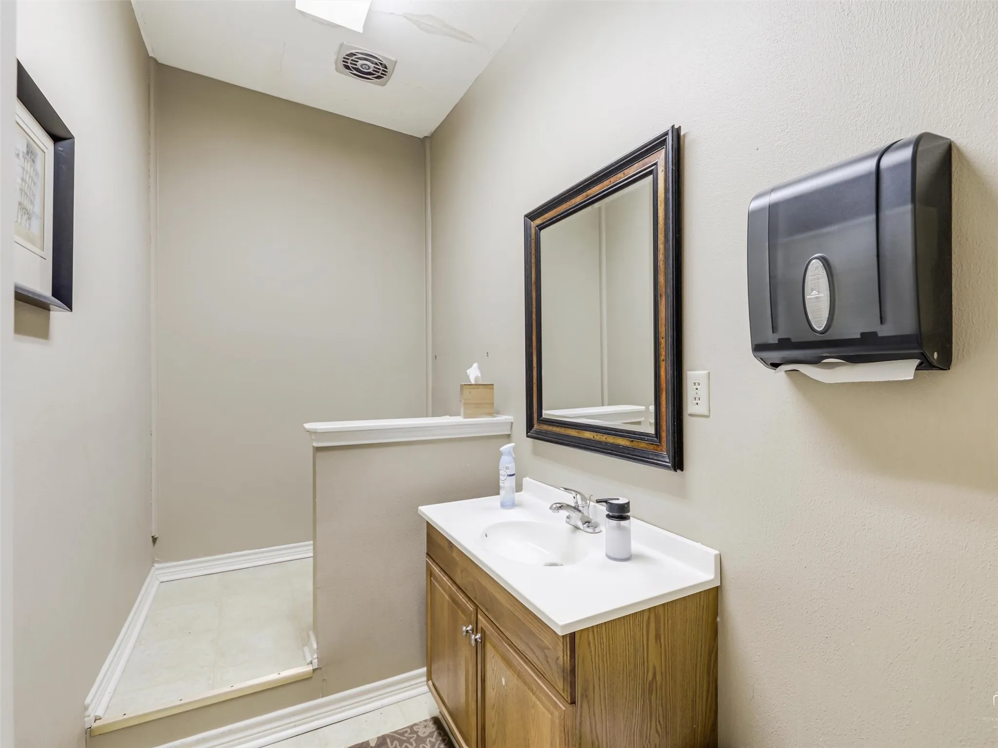 Wood-finish vanity cabinet, integrated sink with chrome faucet, framed wall mirror, and low-profile partition wall