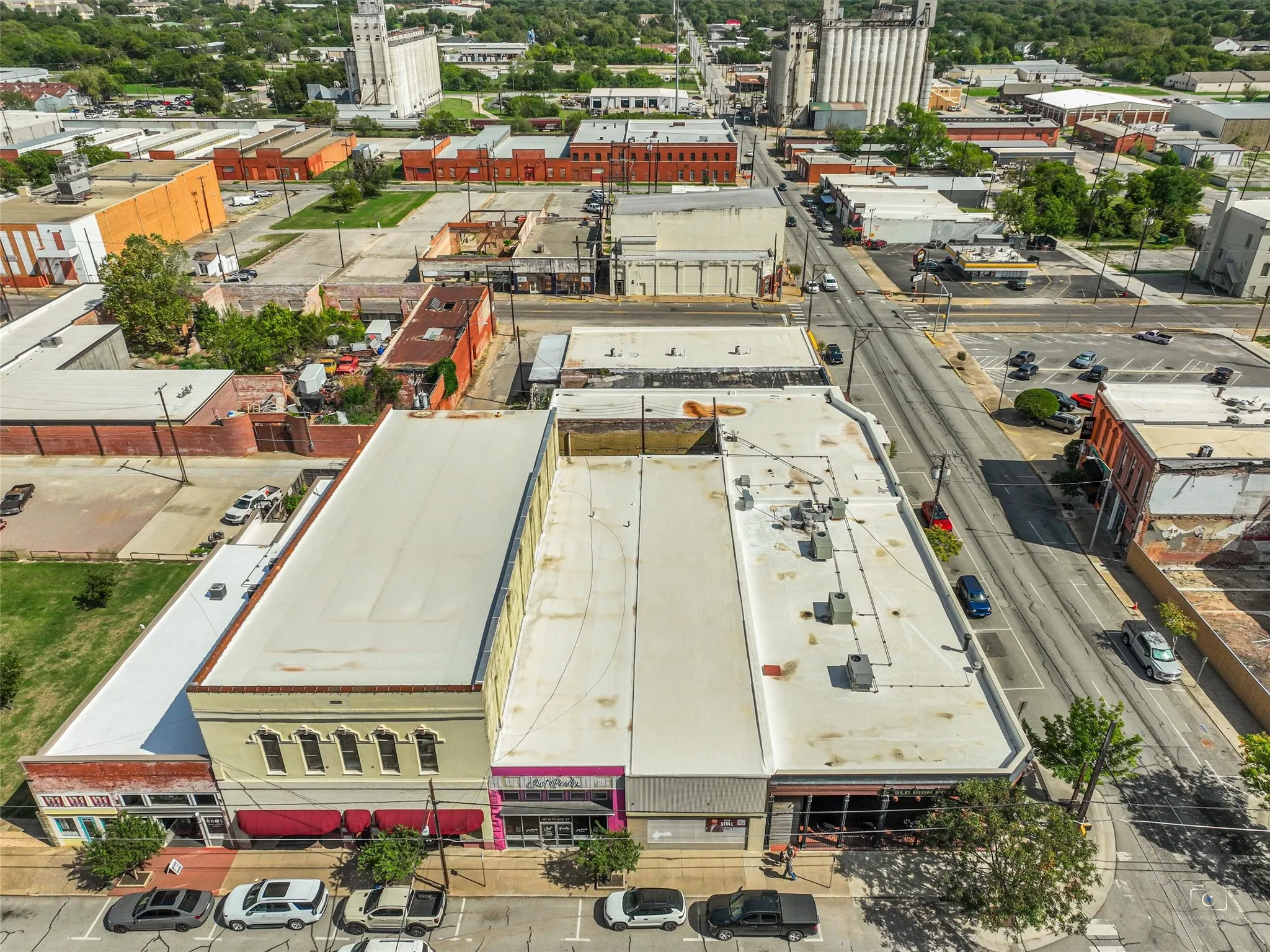 Aerial perspective of commercial property featuring a flat roofline, multi-story masonry facade, ground-level glass storefronts, and on-street parking