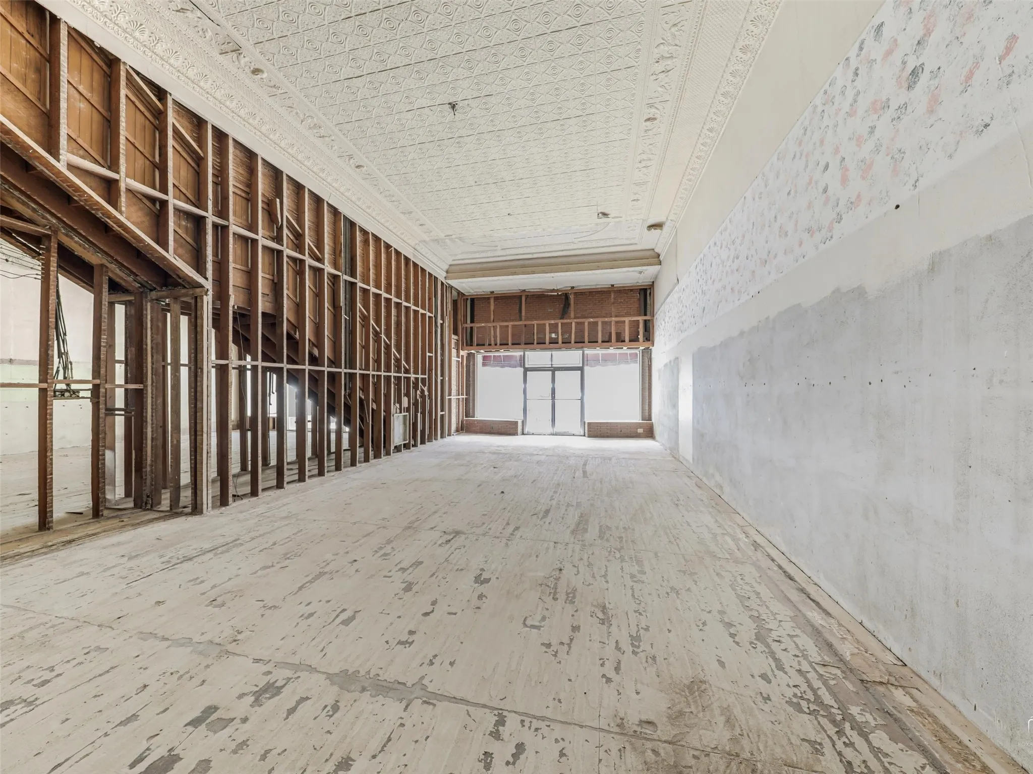 Expansive interior space featuring original stamped metal ceilings with ornate detailing, exposed timber framing, and large street-facing windows