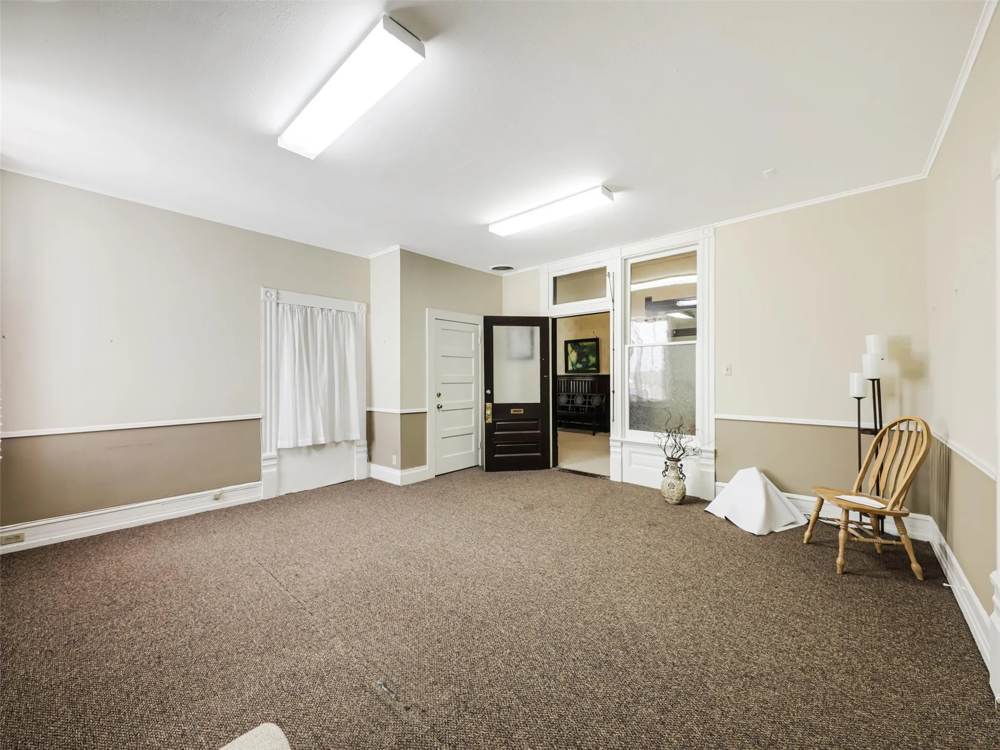 Interior space featuring neutral two-tone wall paint, chair rail molding, carpeted flooring, multi-pane glass-panel door, and dual overhead flush-mount lighting fixtures