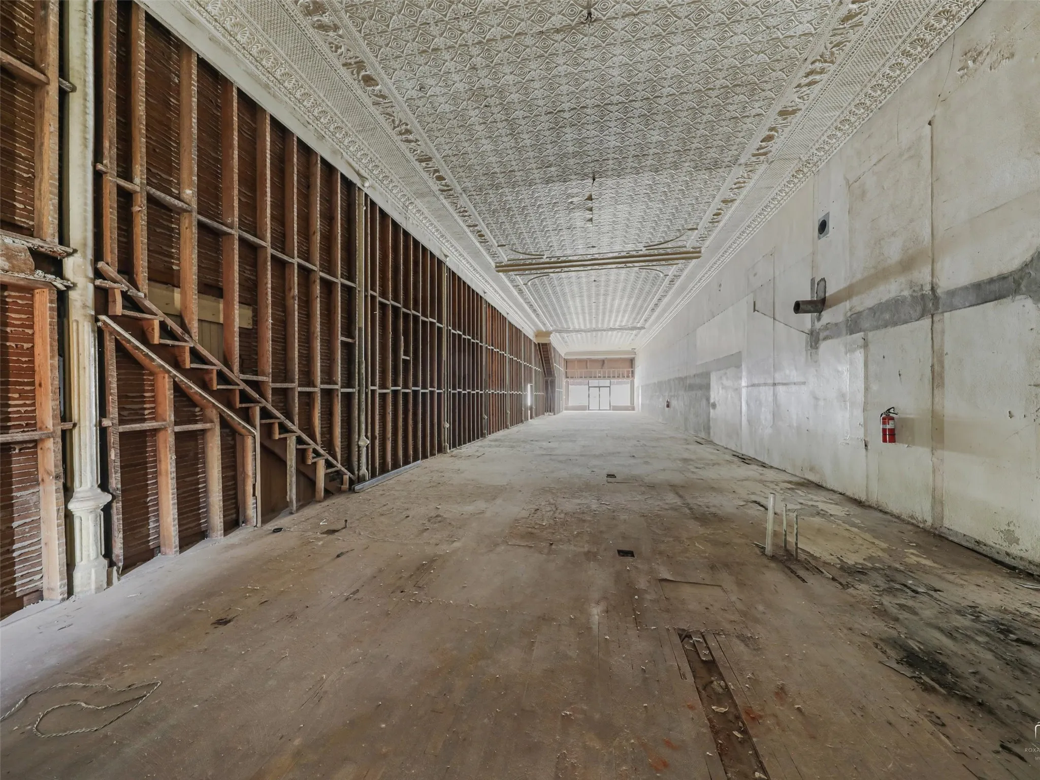 Expansive interior space featuring original decorative pressed metal ceiling, exposed wood framing, and wood-plank flooring