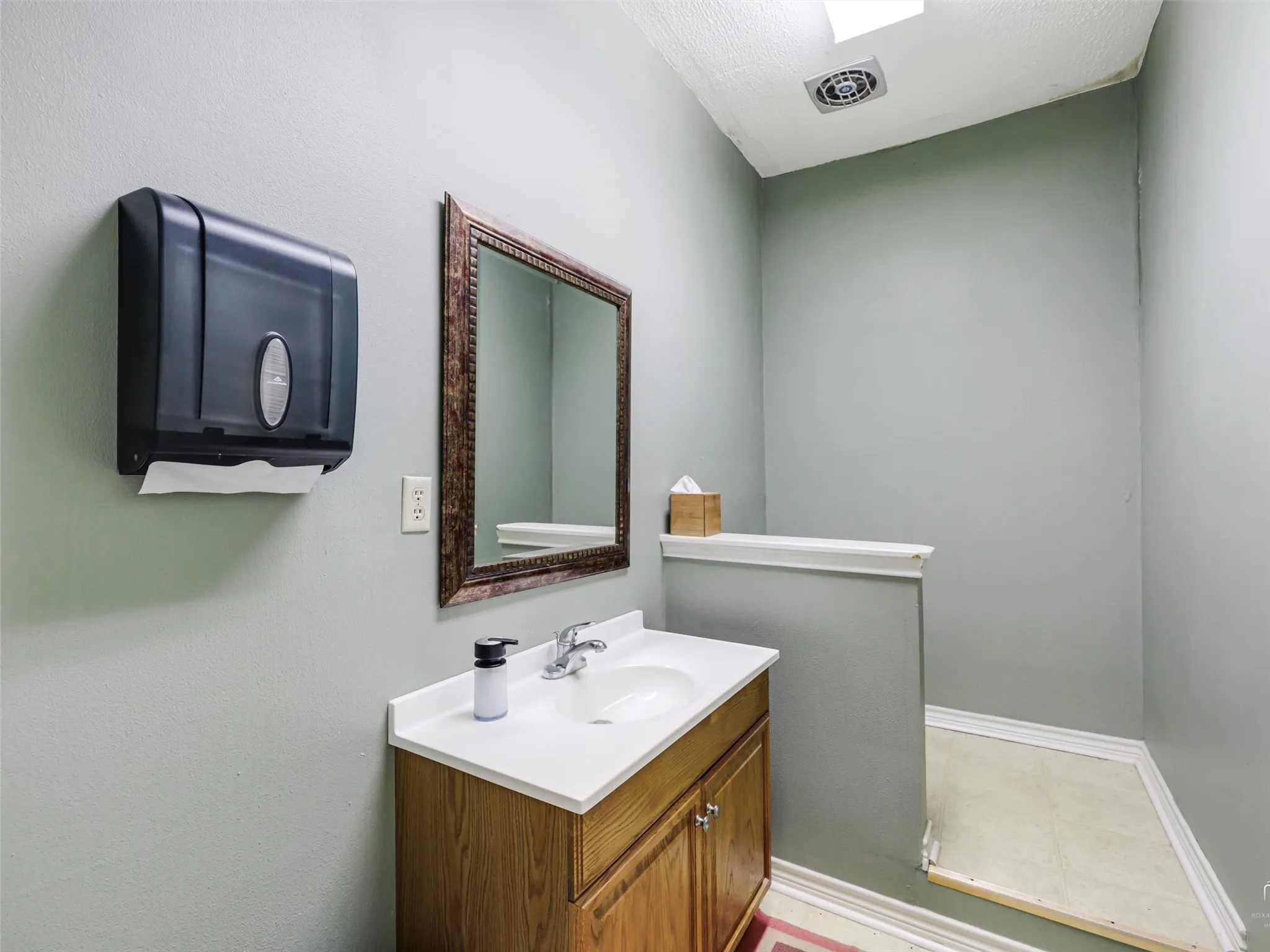 Wood-finish cabinetry, solid-surface countertop with an integrated basin, chrome-finished faucet, and wall-mounted framed mirror