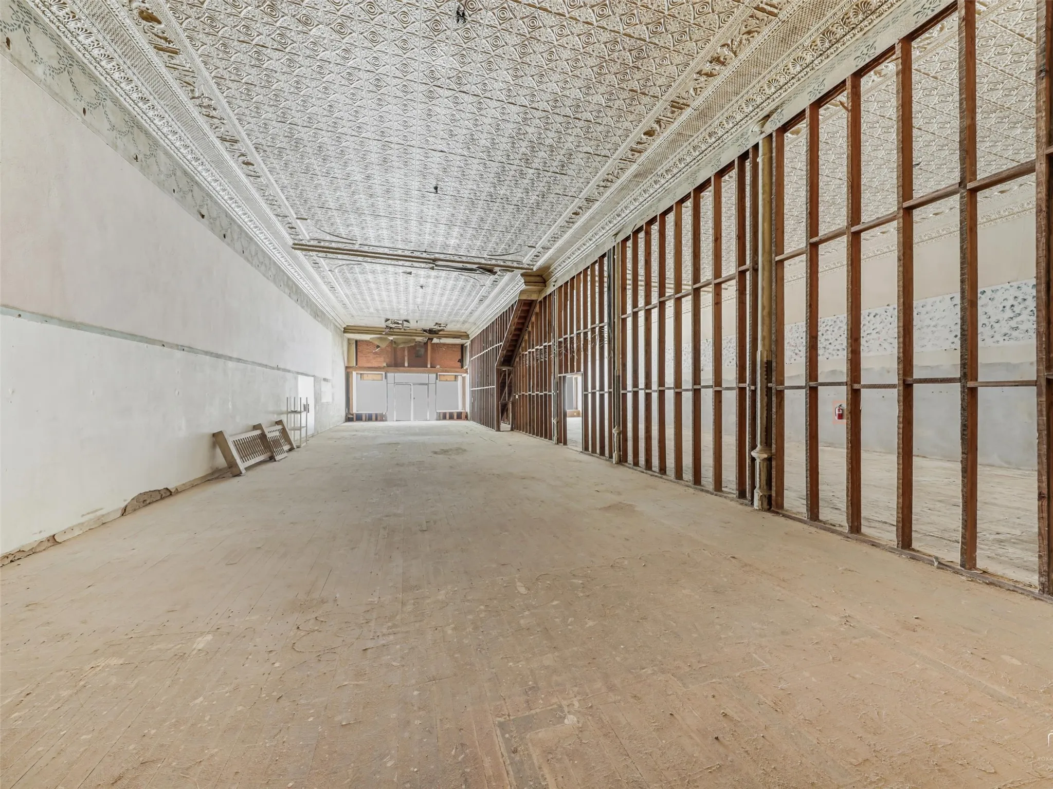 Expansive interior space featuring original patterned tin ceilings, exposed wooden wall framing, and open floor plan