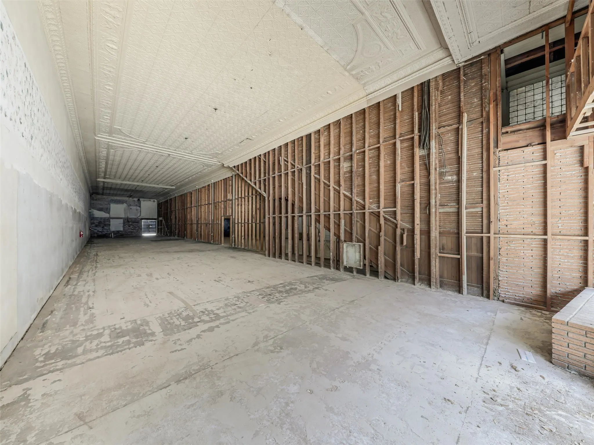 Expansive open-concept interior featuring an ornate pressed tin ceiling, exposed timber stud wall framing, and concrete flooring