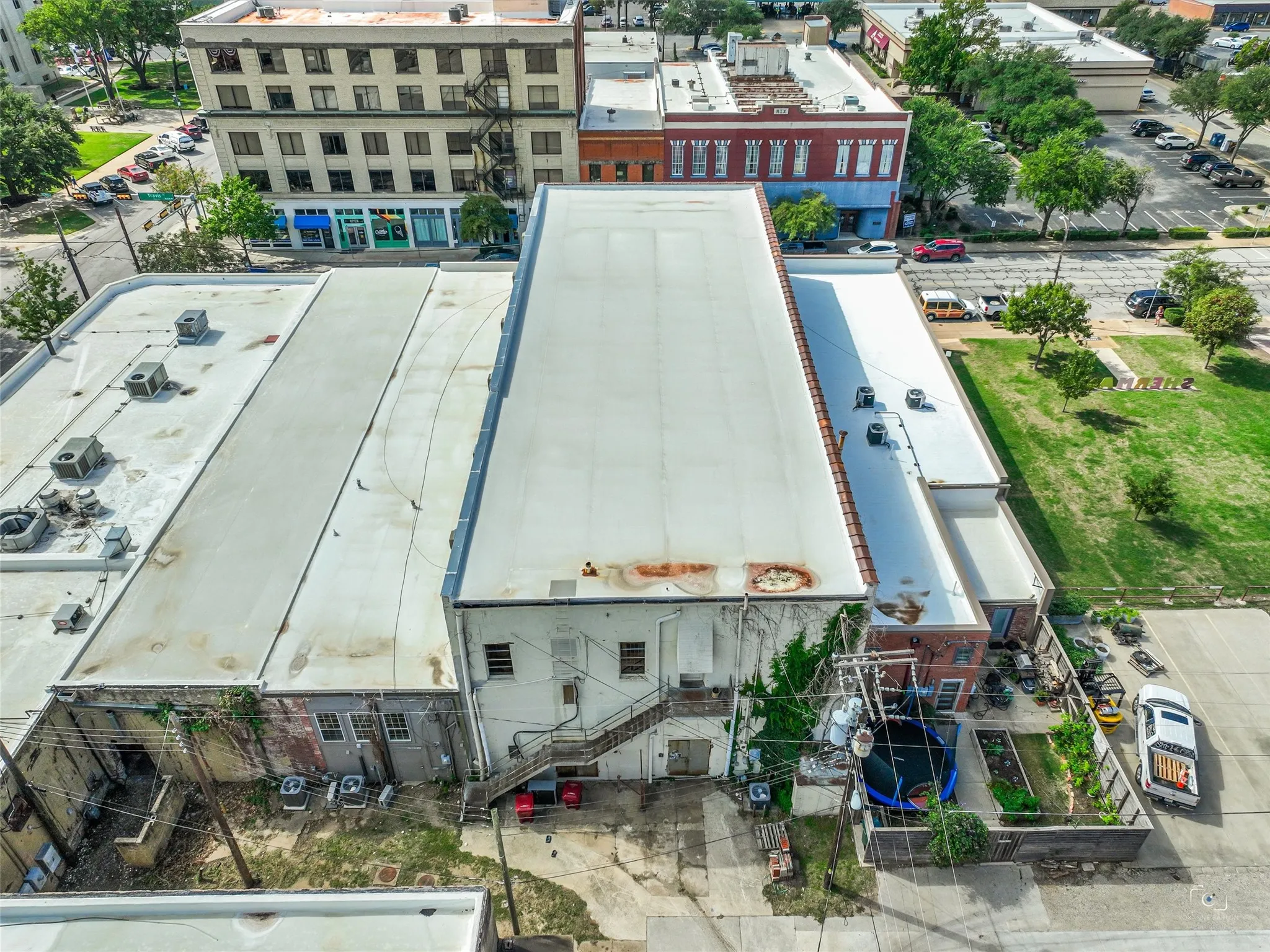 Aerial view of a multi-level structure featuring a flat roofing system, exterior metal staircase, masonry wall construction, and paved ground-level lot
