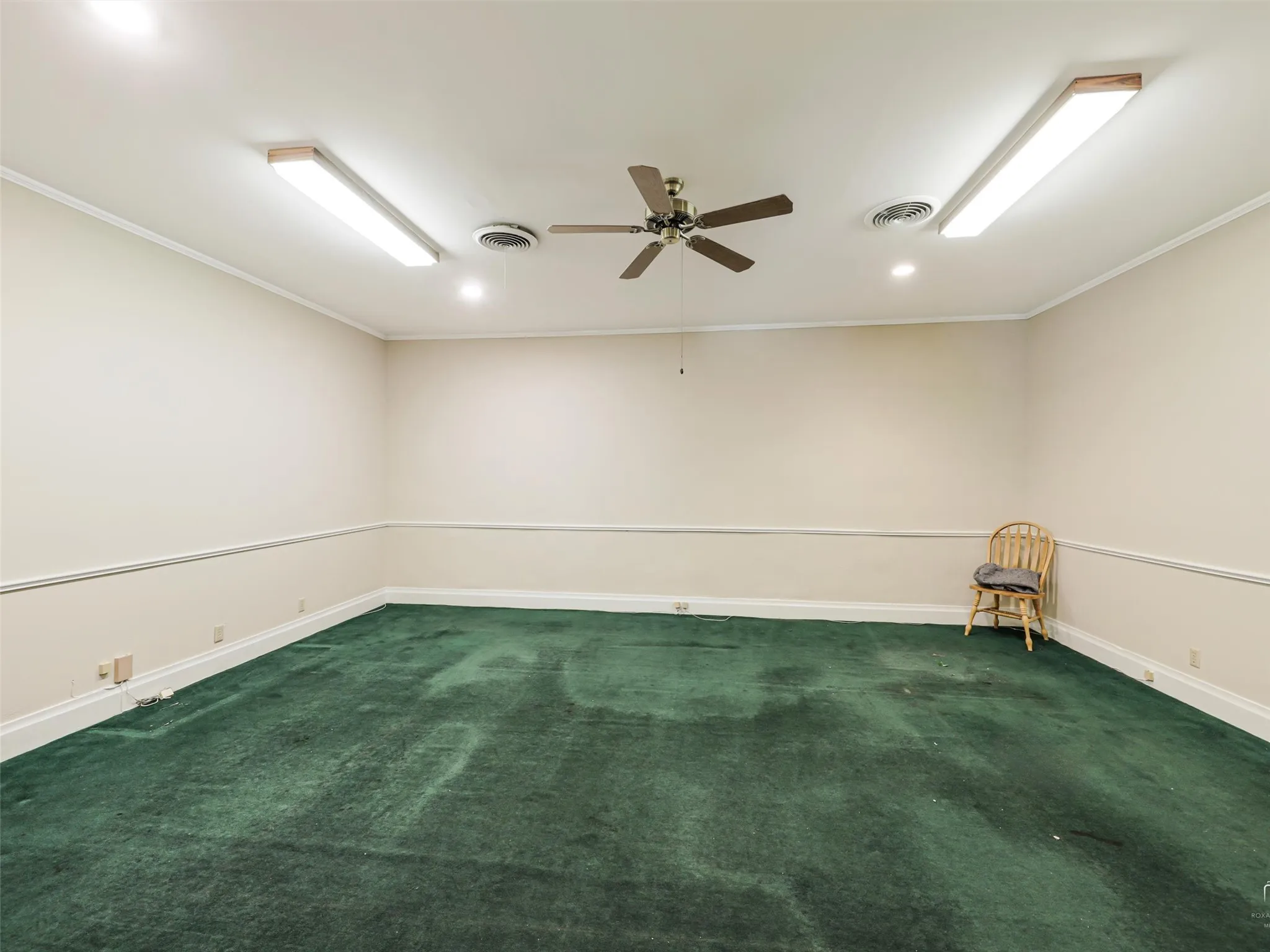 Expansive room featuring wall-to-wall carpeting, chair rail molding, ceiling fan, and dual recessed linear lighting fixtures