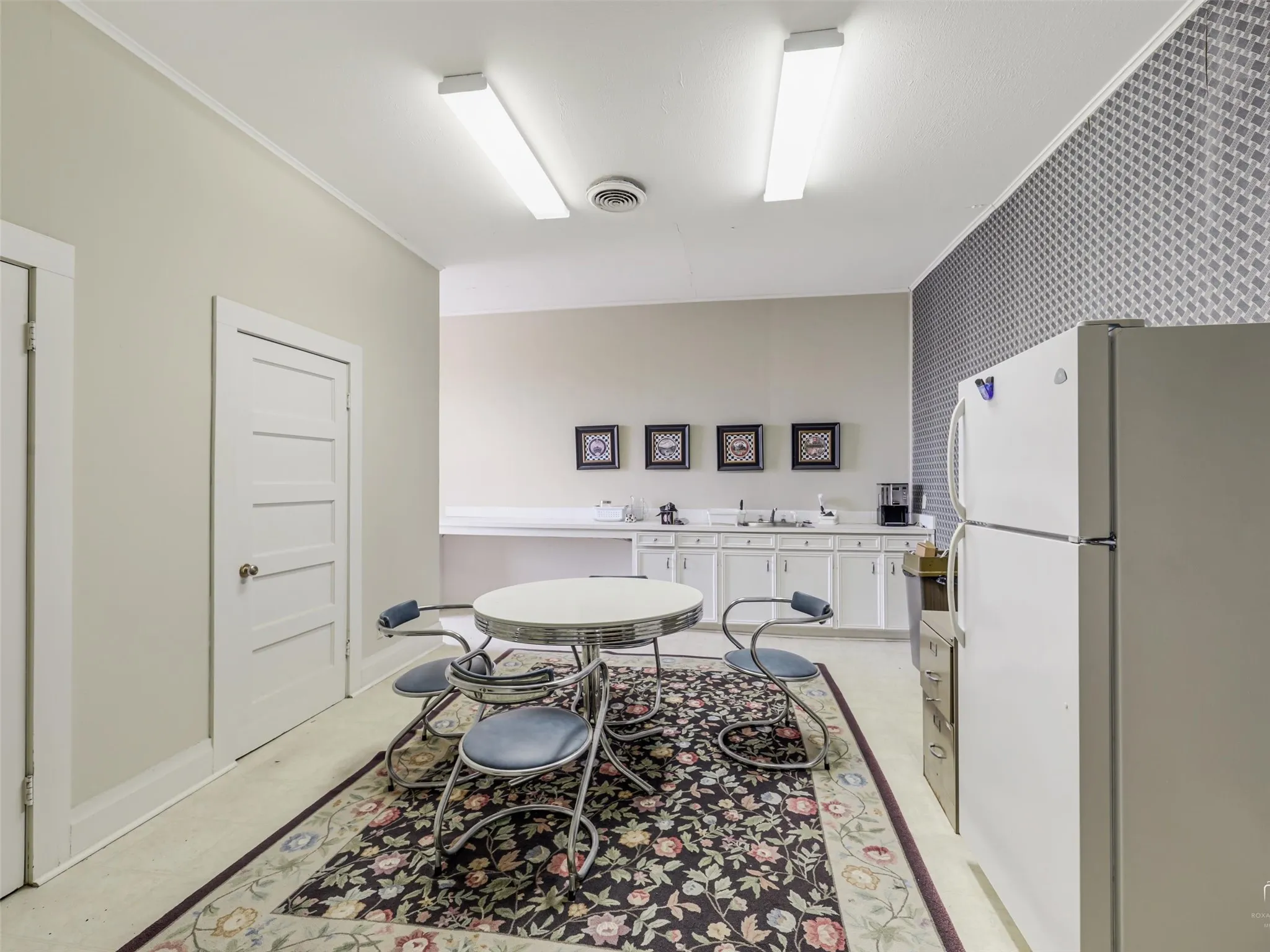 Kitchen area featuring white cabinetry, a built-in countertop, patterned wall surfacing, and dual linear light fixtures