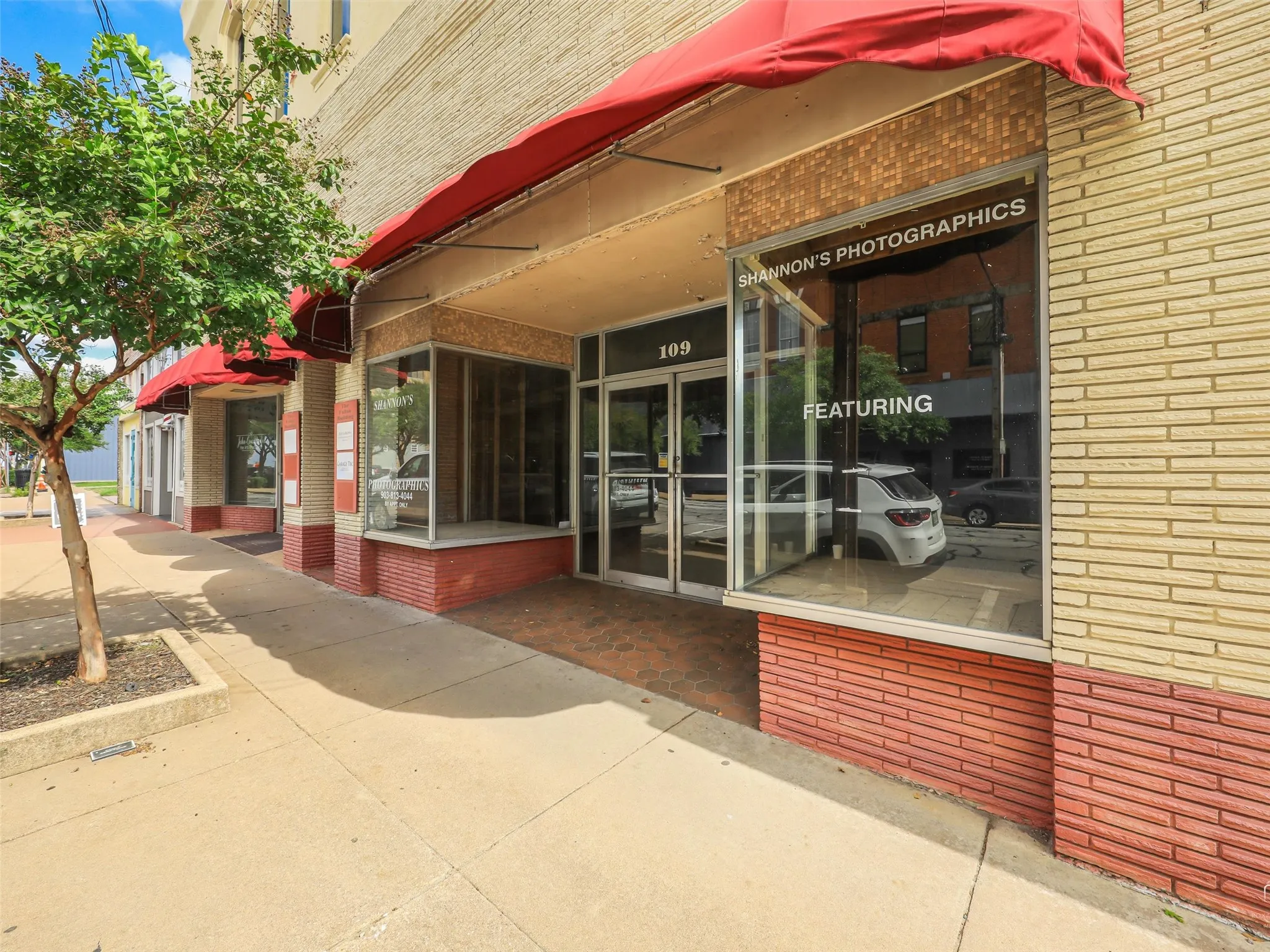 Commercial exterior featuring a brick facade, recessed glass storefront entrance, large display windows, and fabric awnings