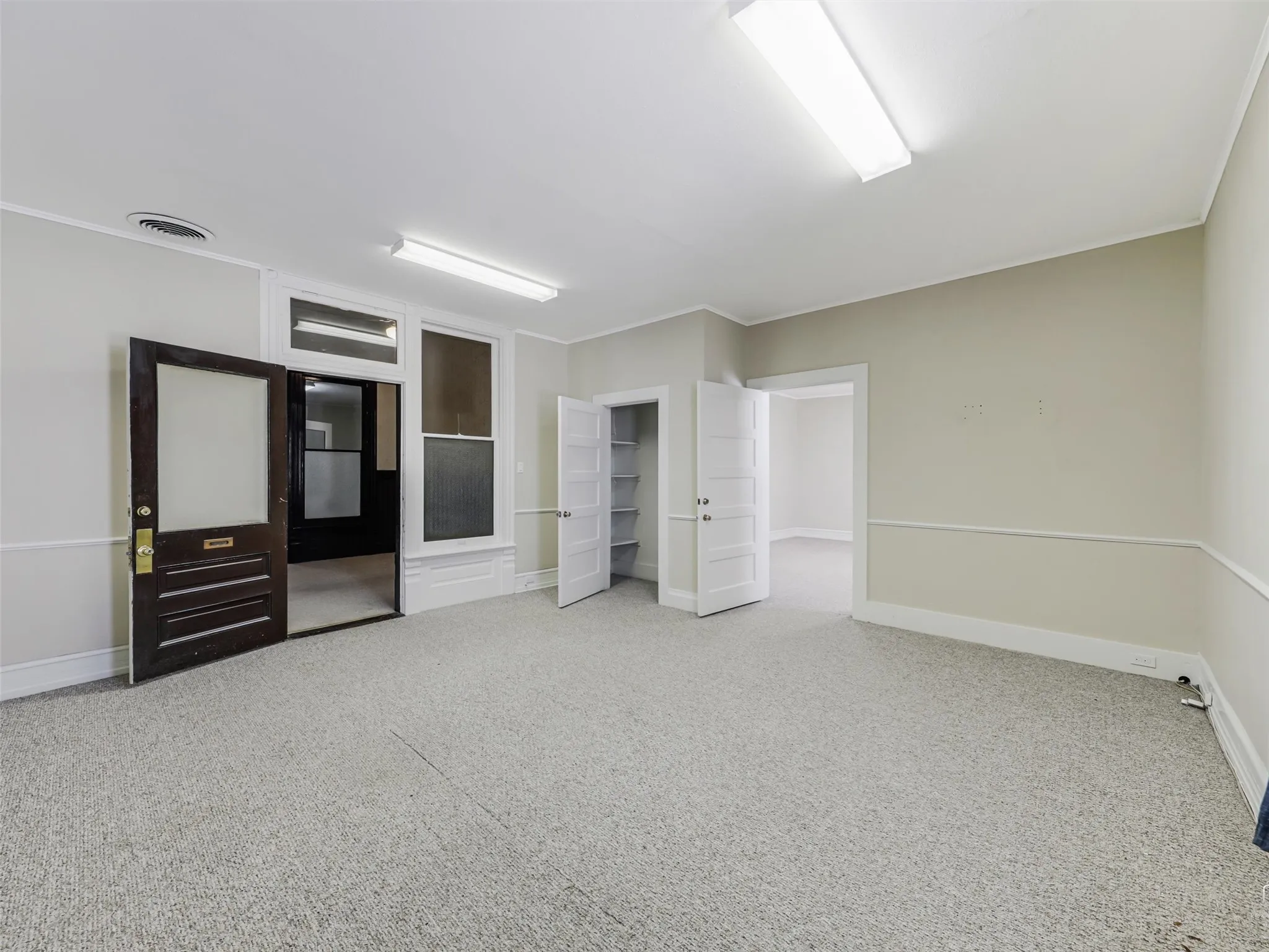 Interior room featuring neutral wall color, chair rail molding, carpet flooring, a dark-finished wooden door with a glass pane, and built-in closet shelving