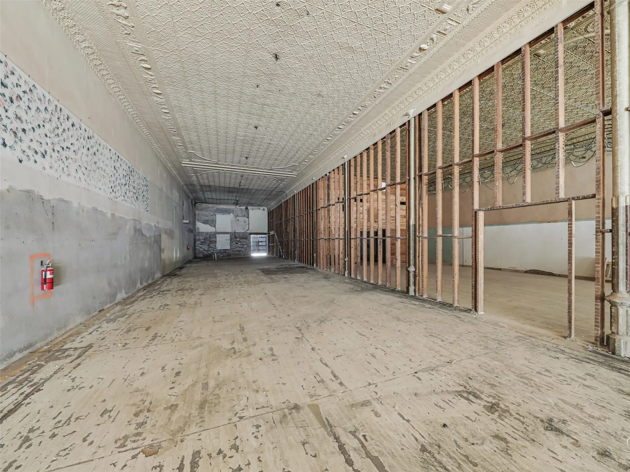 Expansive interior space featuring ornate pressed tin ceilings, exposed wall stud framing, and a metal support column