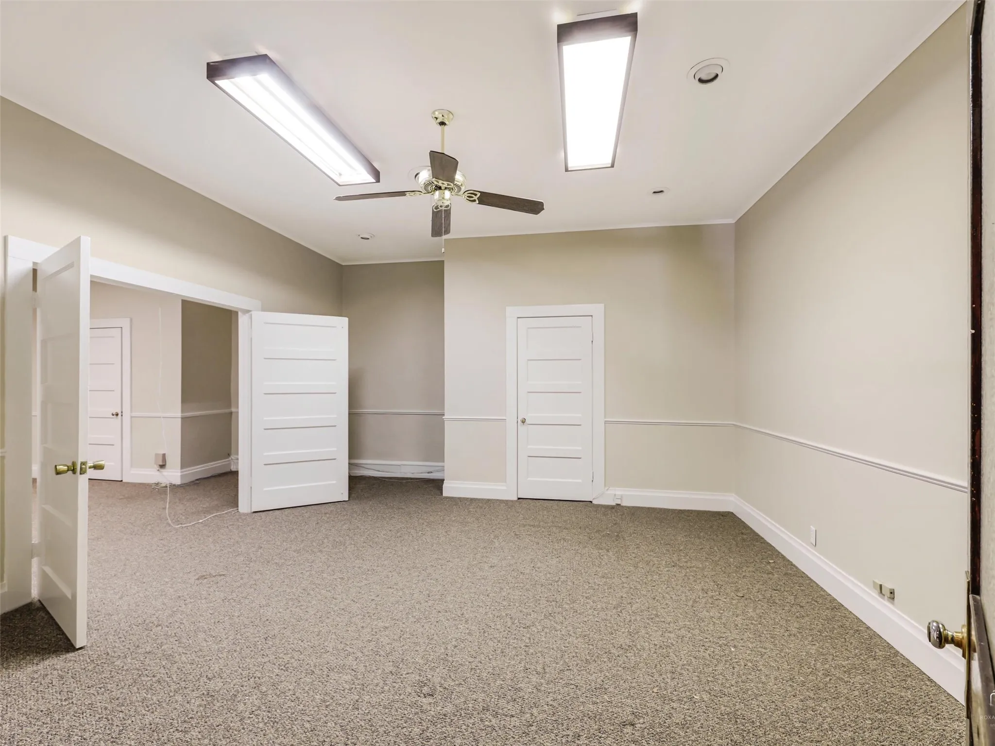 Interior room featuring neutral wall paint, chair rail molding, ceiling-mounted light fixtures, and a center ceiling fan