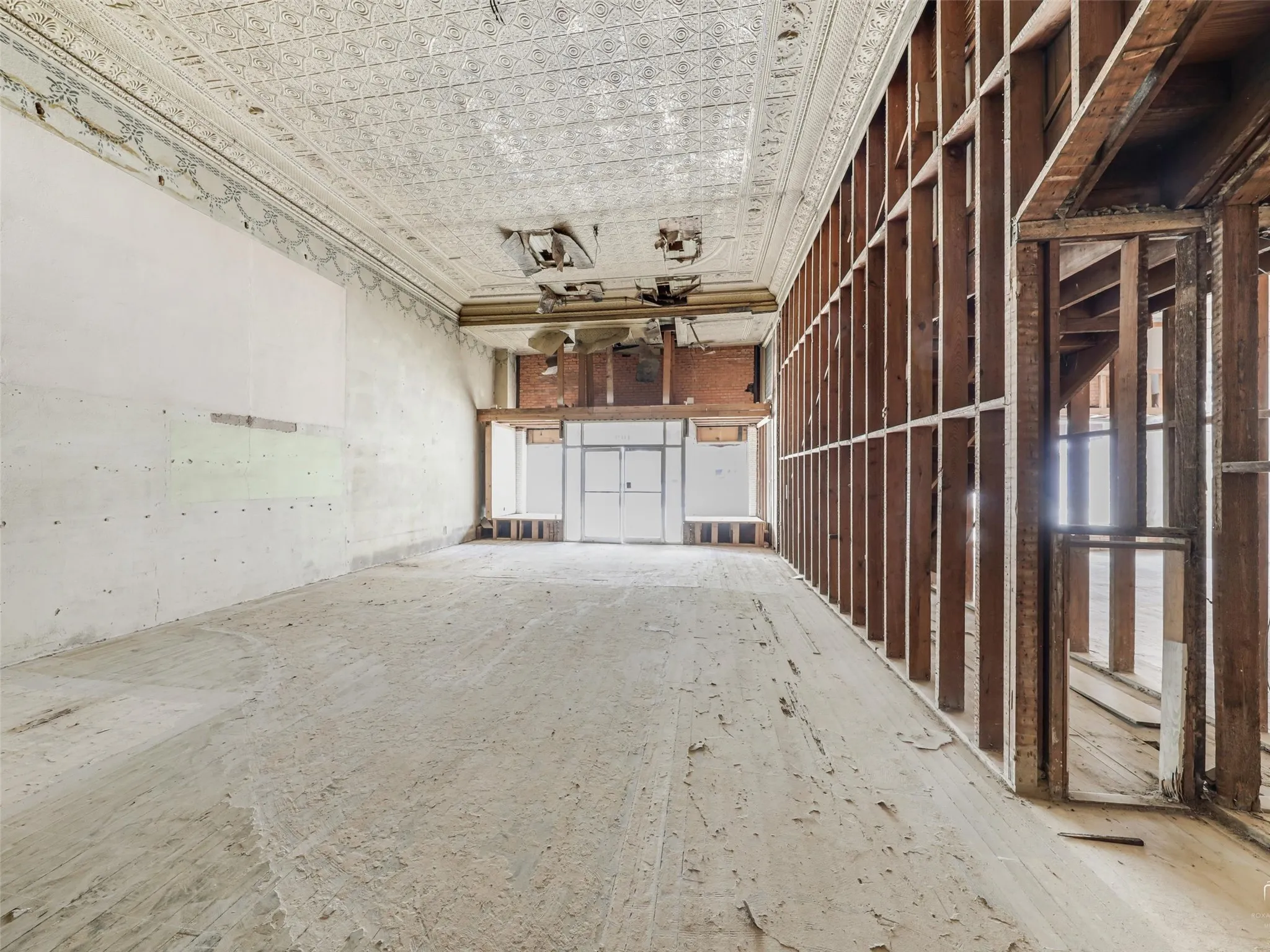 Open interior space featuring an ornate pressed tin ceiling, exposed wood stud wall framing, masonry wall construction, and storefront entry glass