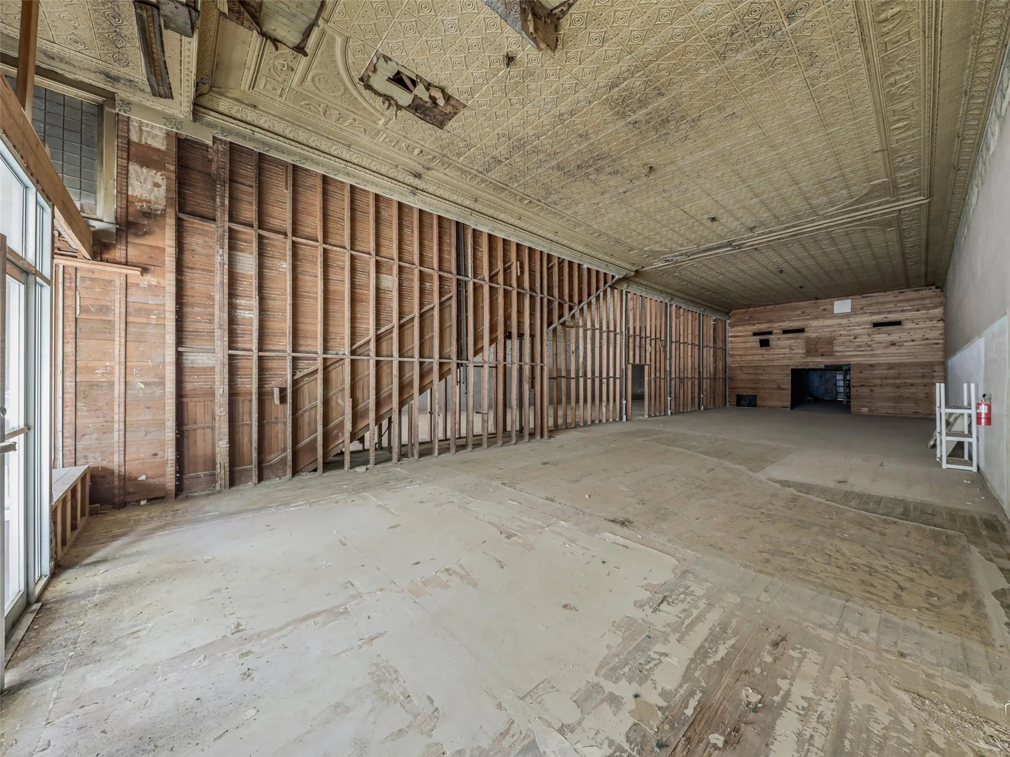 Expansive interior space featuring original stamped metal decorative ceiling, exposed wood stud wall framing, and high ceilings