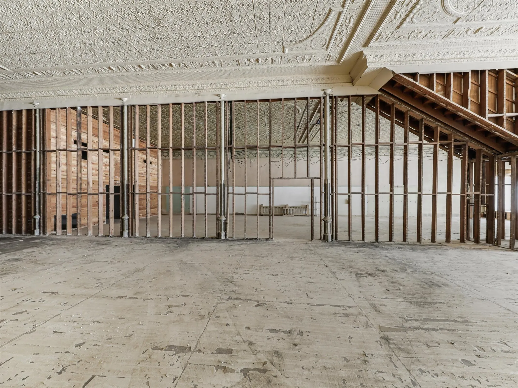 Expansive interior space featuring original ornate tin ceiling panels, exposed wooden wall stud framing, and structural metal support columns