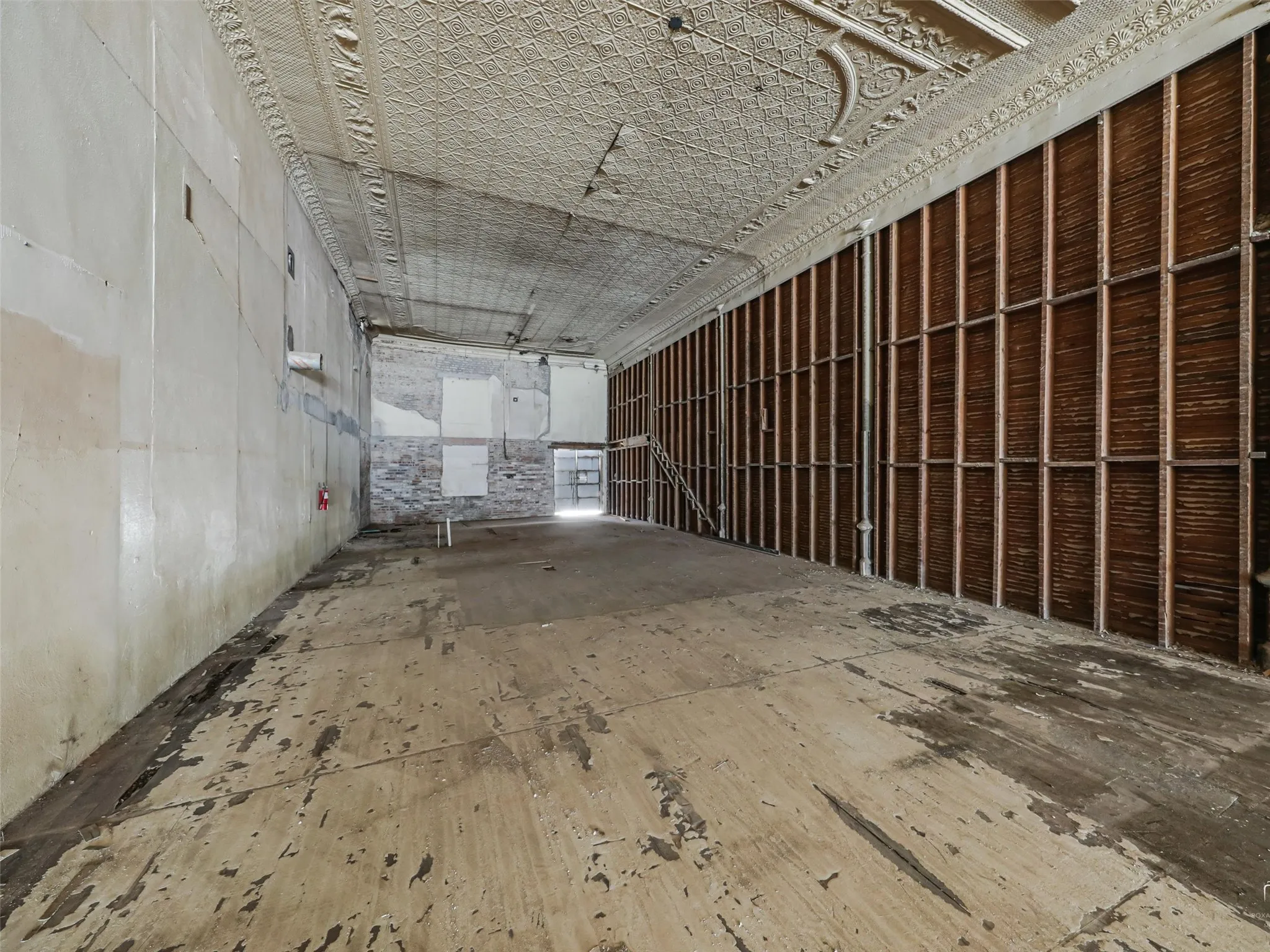Expansive open-concept interior featuring an ornate, pressed-tin ceiling, exposed brick wall segments, and a timber-frame wall structure