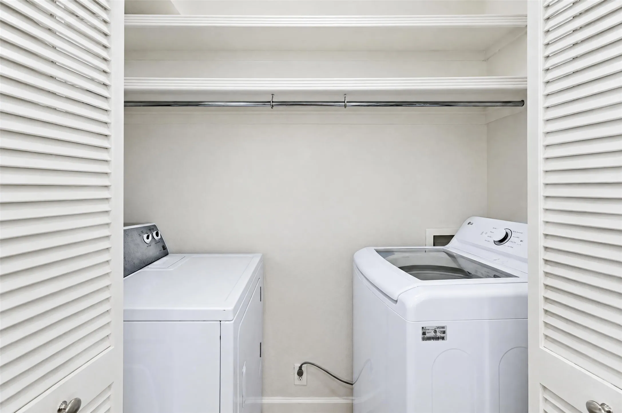 Laundry closet featuring louvered bi-fold doors, dual built-in overhead storage shelves, and a metal garment rod