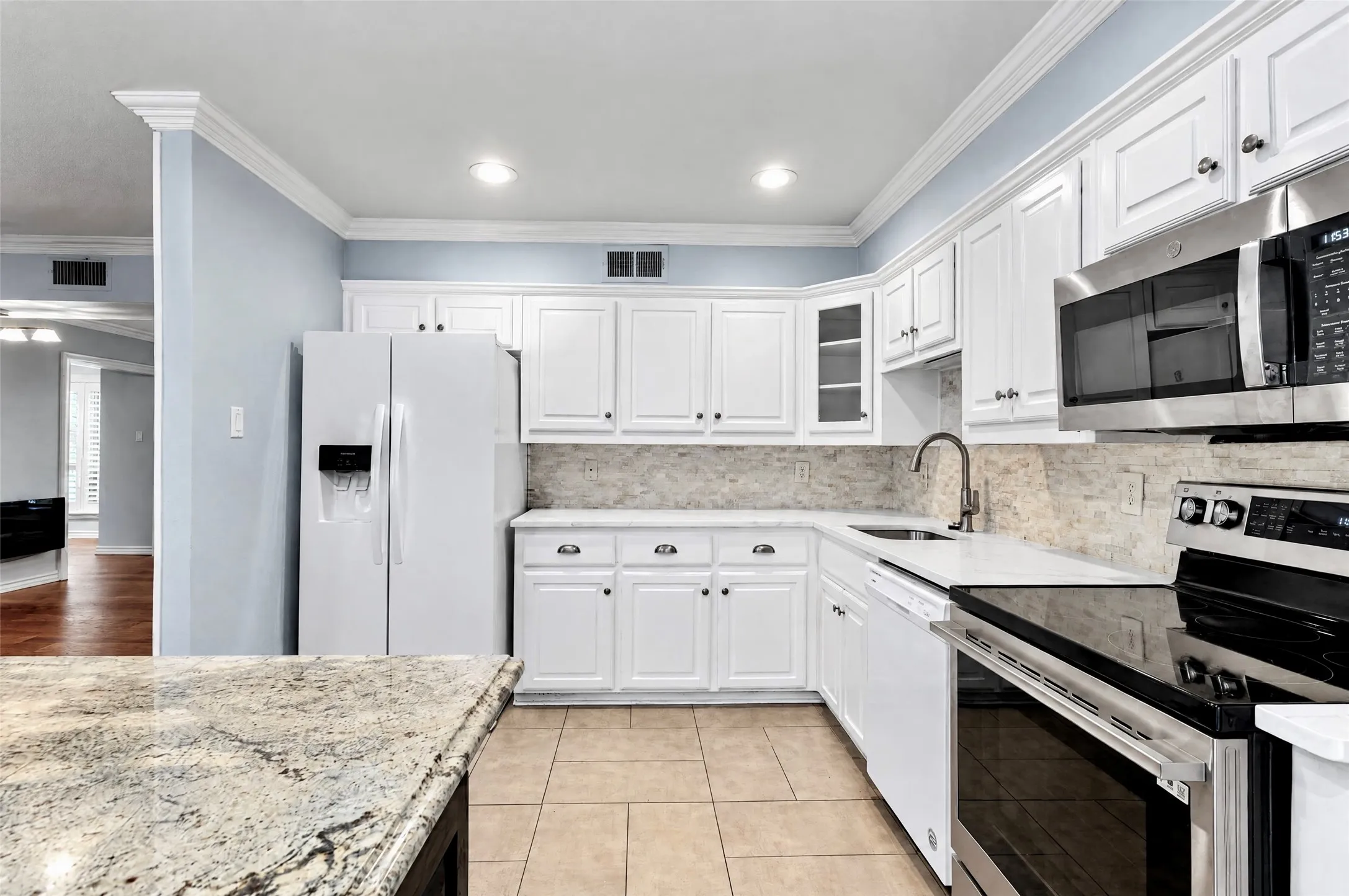 Kitchen featuring white shaker-style cabinetry, stone-finish countertops, stainless steel appliances, tiled backsplash, and recessed lighting
