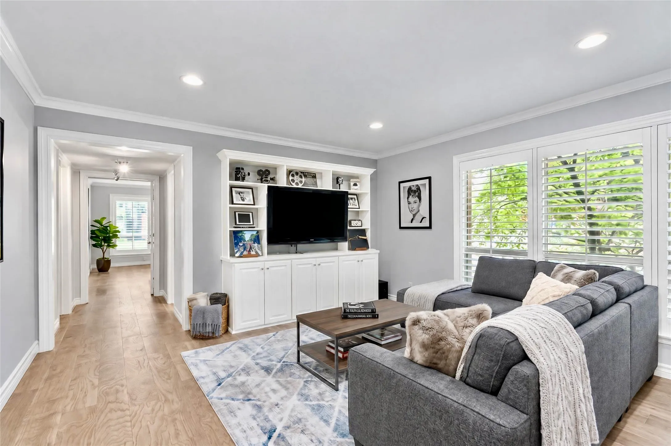 Living space featuring wood-finish flooring, recessed lighting, crown molding, built-in cabinetry, and white louvered window shutters